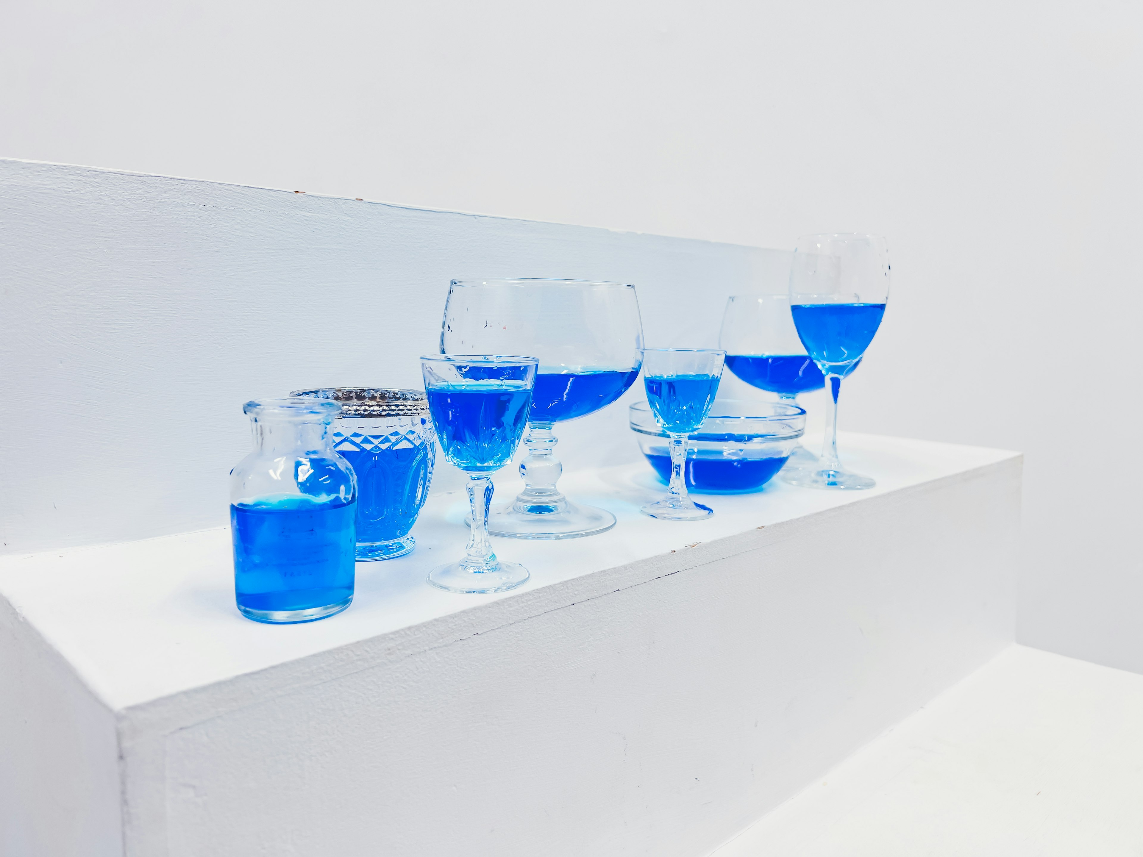 Différents verres remplis de liquide bleu disposés sur une surface blanche