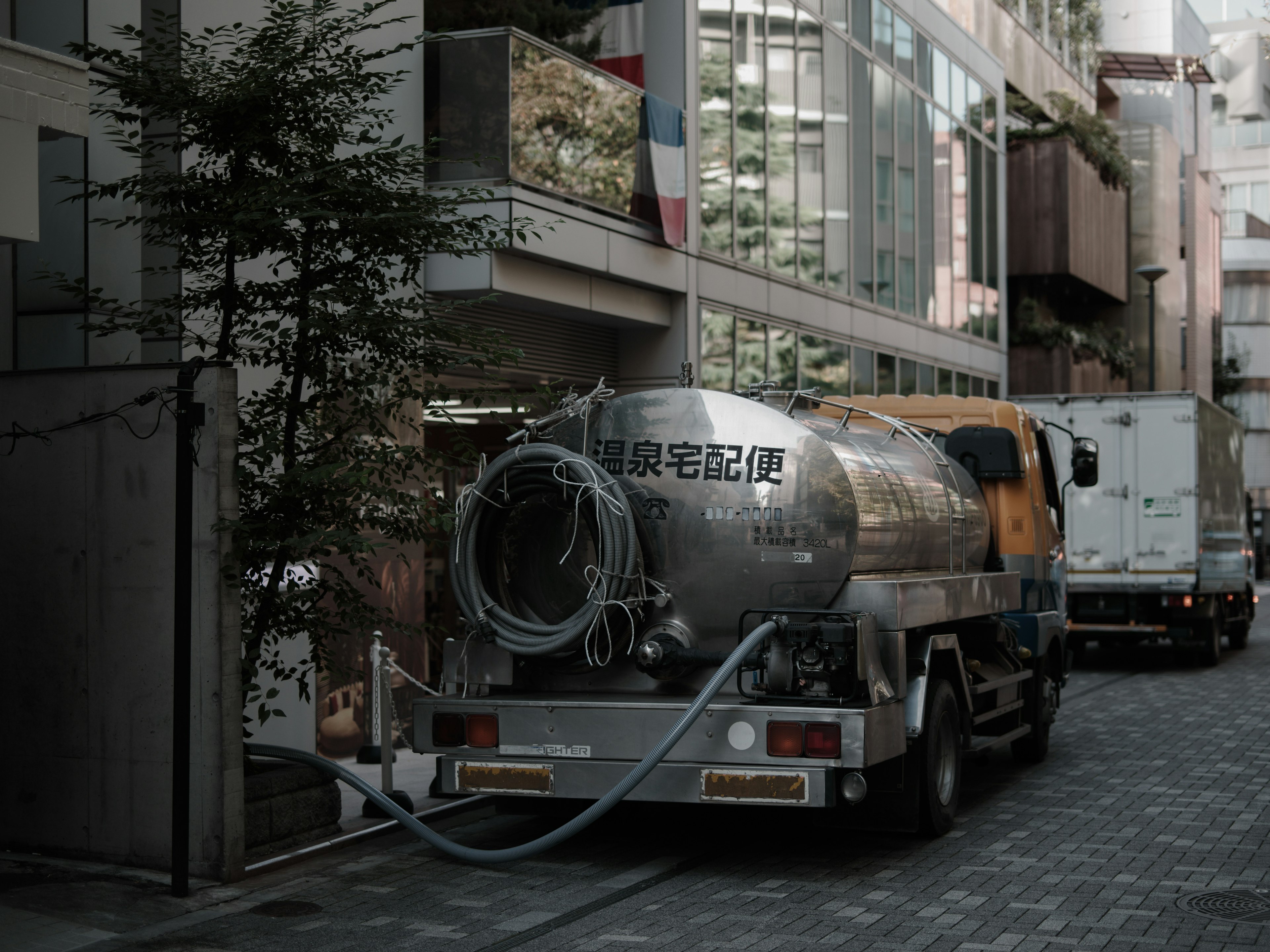 A silver tanker truck parked on a narrow street with modern buildings in the background