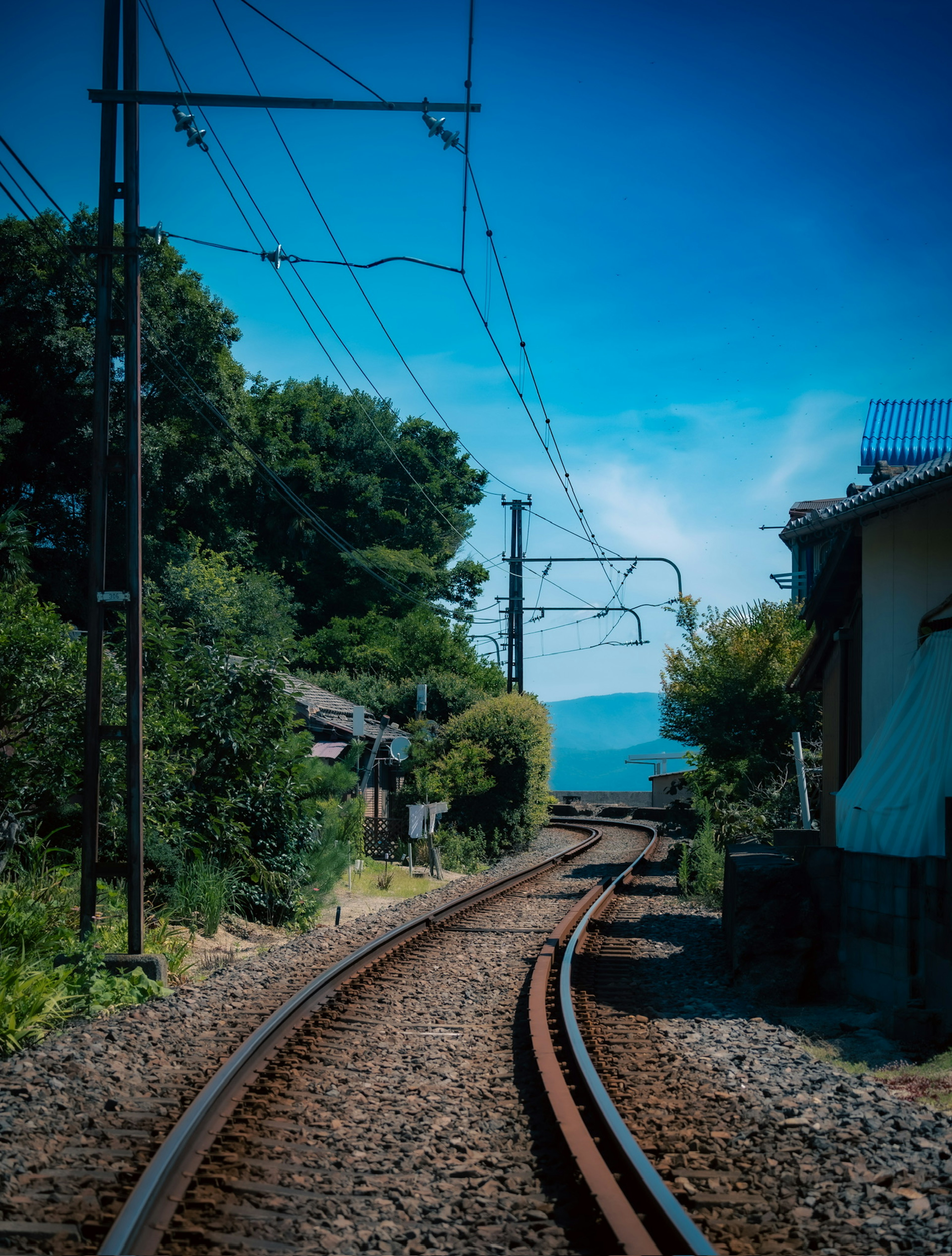 รางรถไฟโค้งที่มีต้นไม้เขียวขจีและบ้านอยู่ข้างๆ