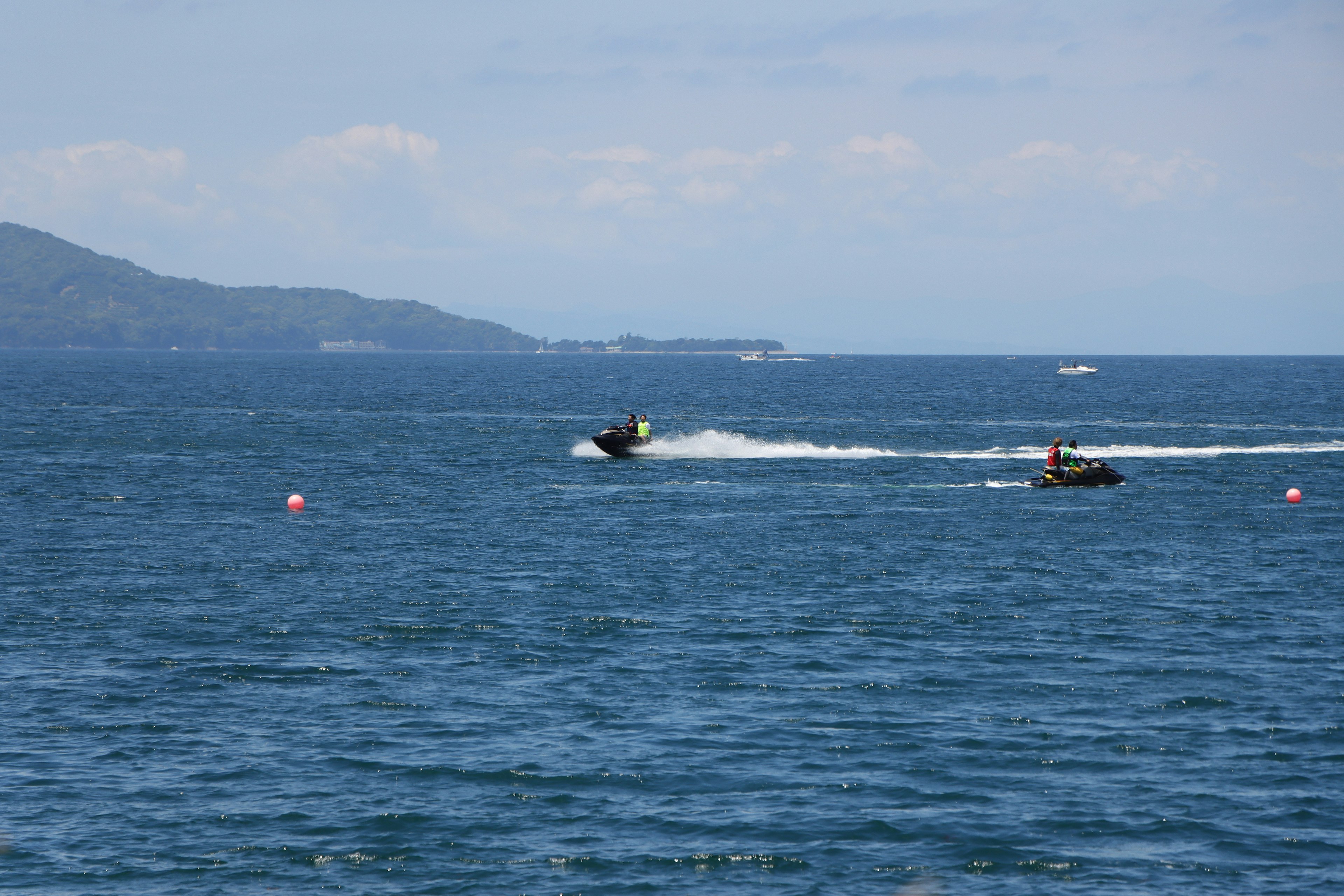 Two jet skis racing on a blue ocean with distant mountains