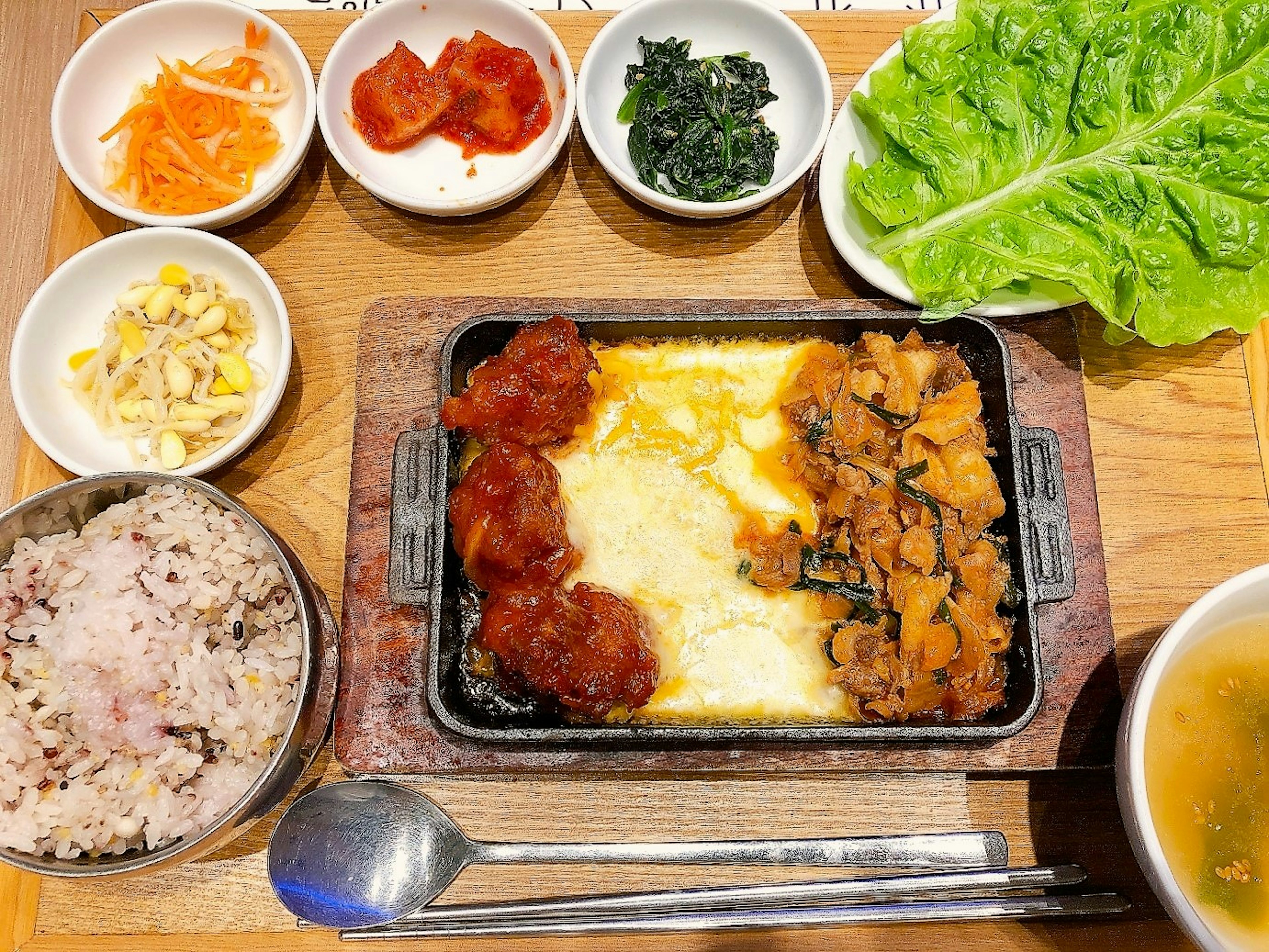 Sizzling dish with rice set featuring side dishes of vegetables and kimchi with fresh vegetable arrangement