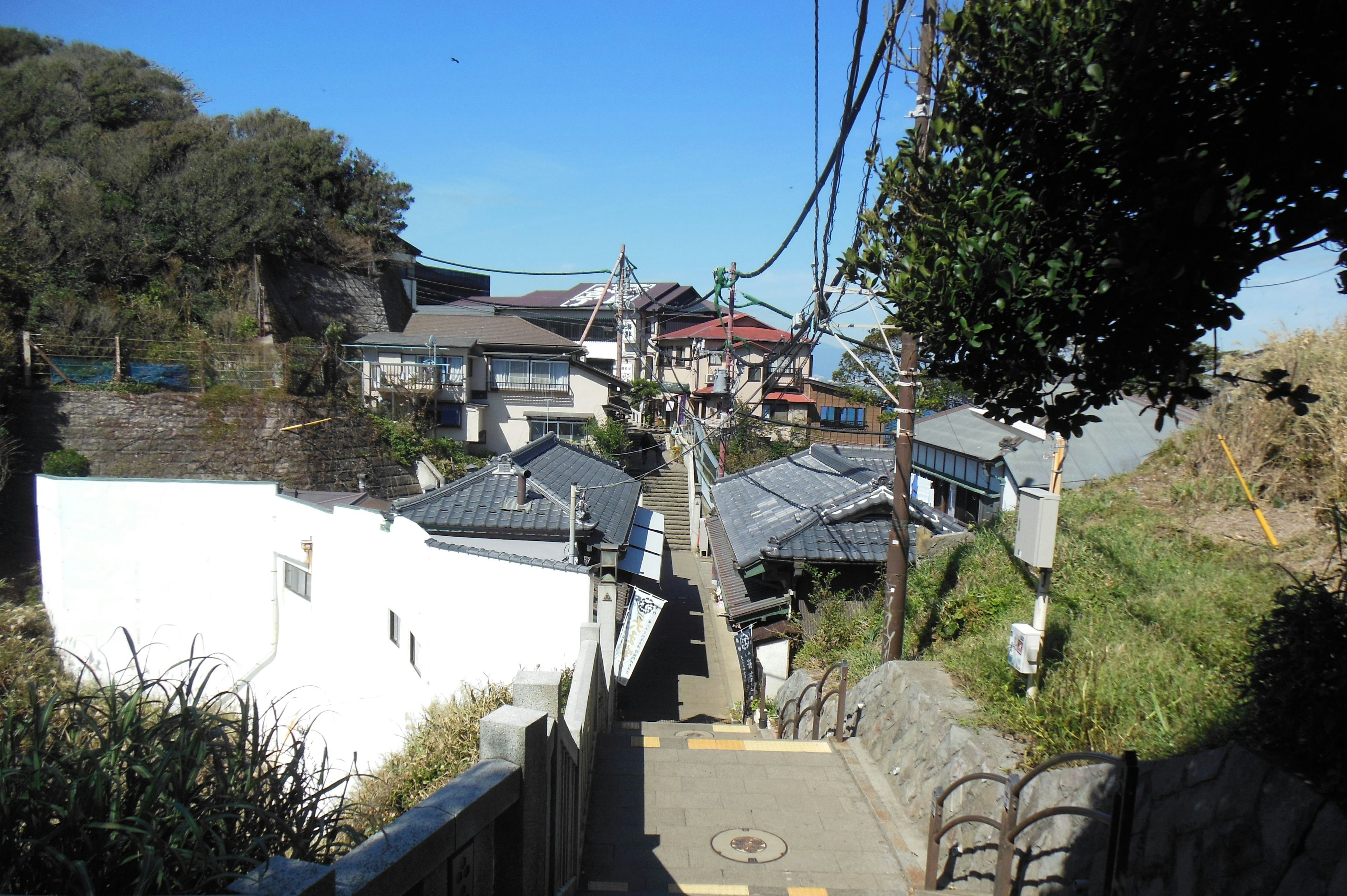 静かな街並みの風景、青空、白い壁の家々、電線、緑の木々