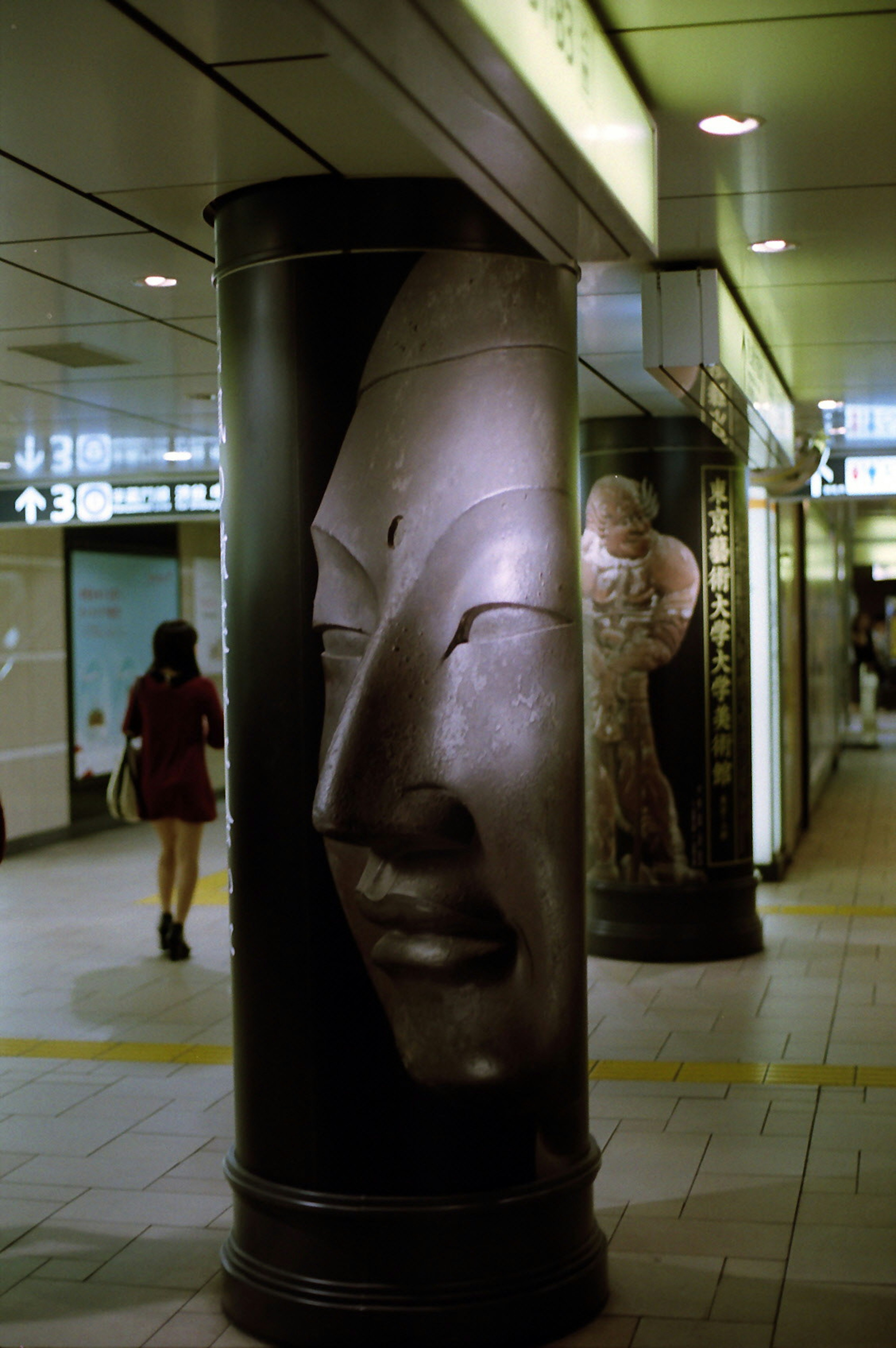 Diseño de cara esculpida en un pilar de estación de metro con un transeúnte