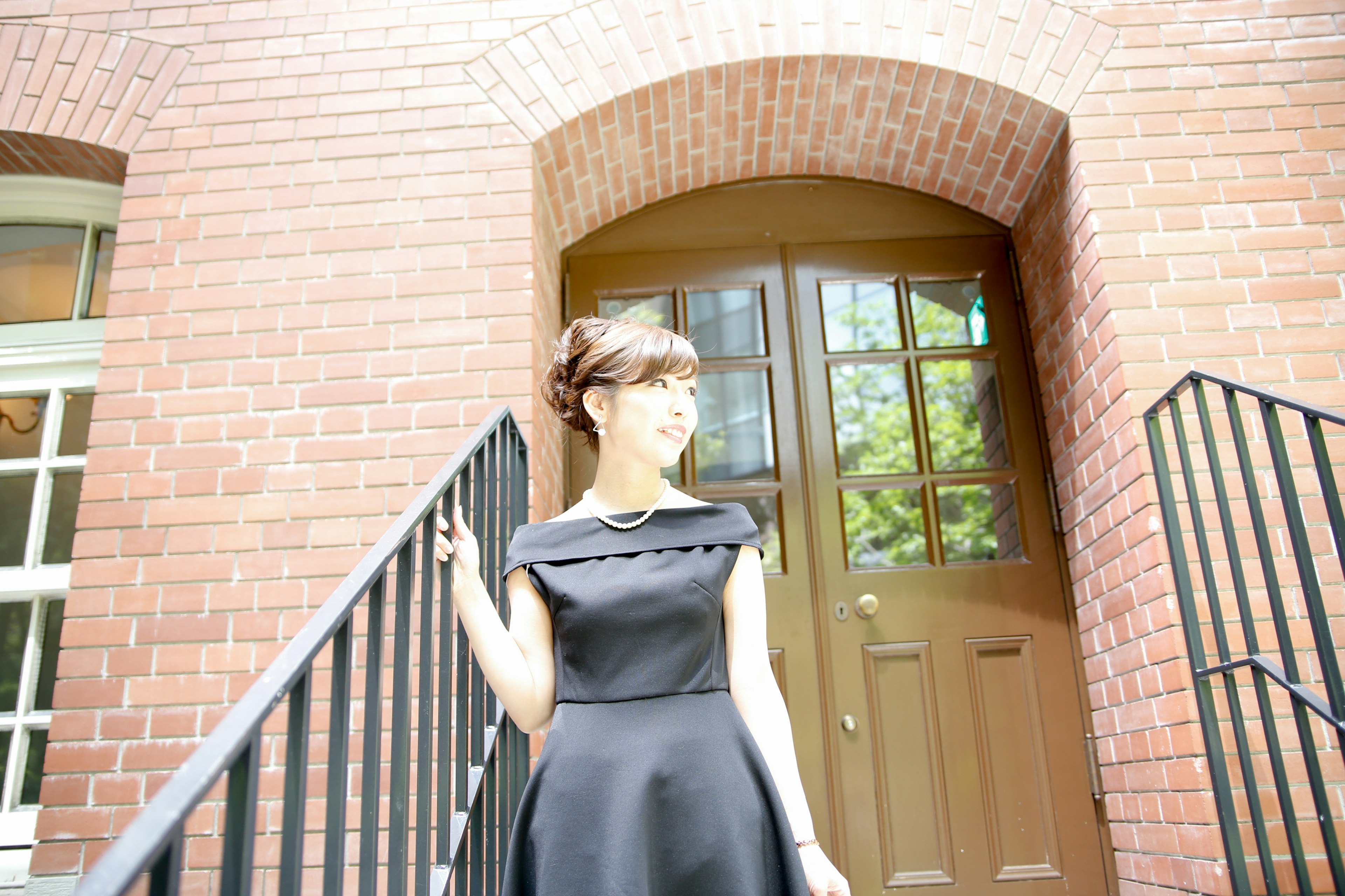 A woman in a black dress ascending the stairs of a brick building