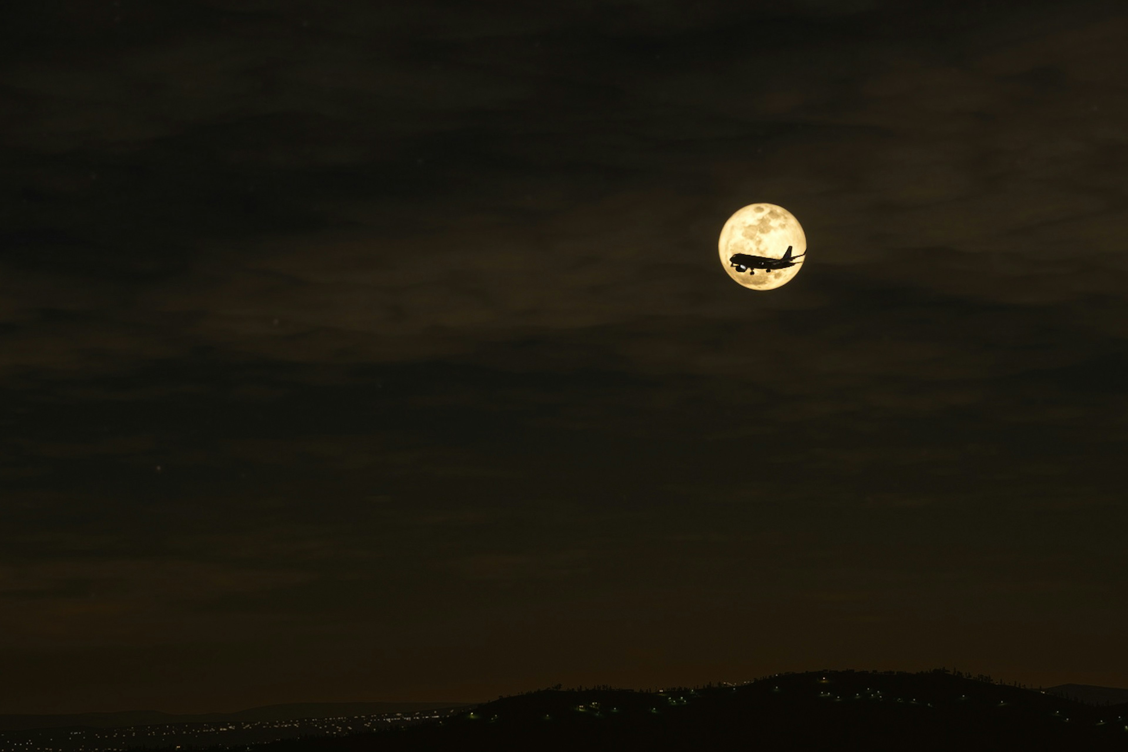 Bulan purnama besar di langit malam dengan siluet pesawat terbang di depannya