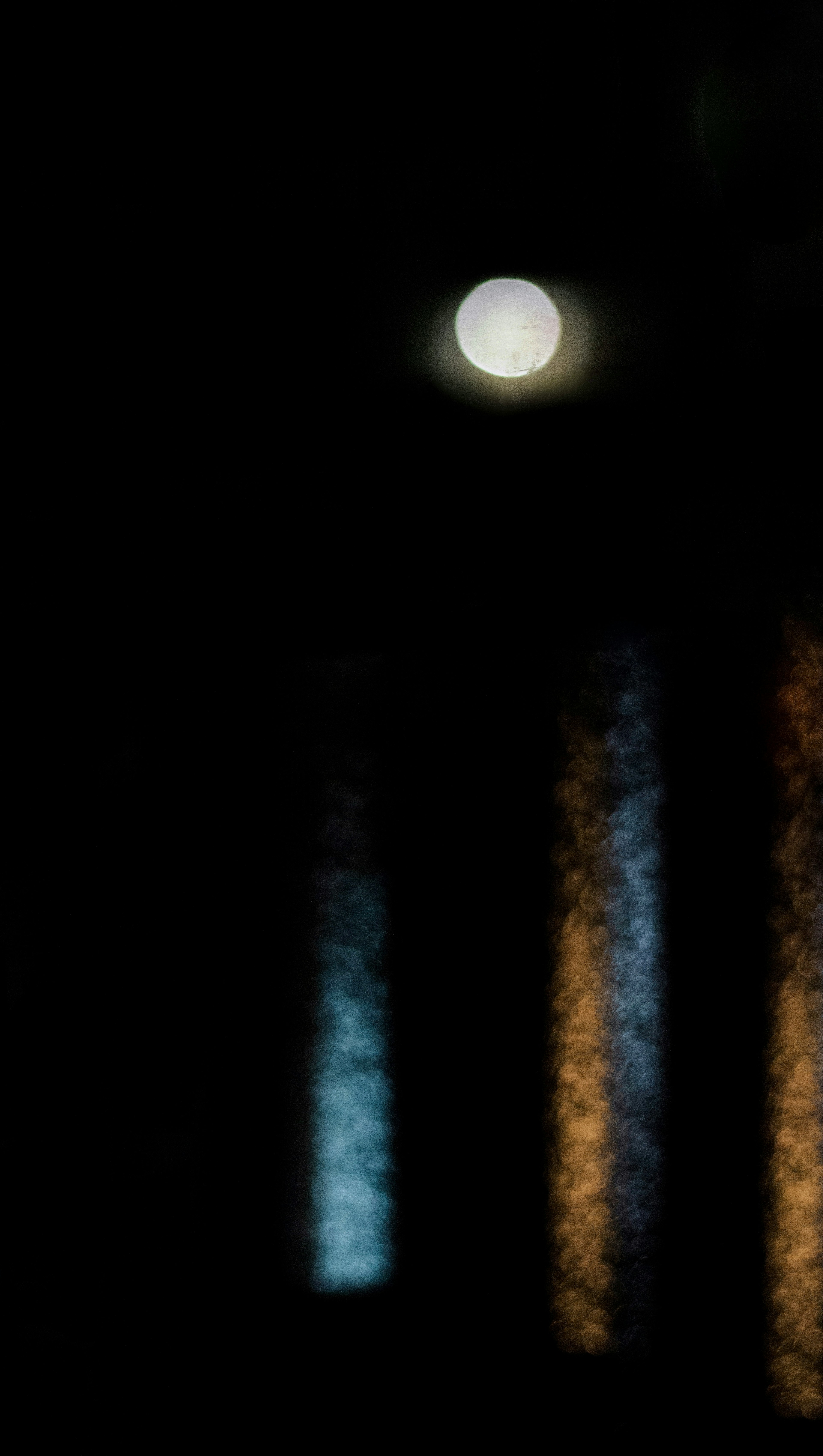 Faint moon against a dark background with colorful light reflections