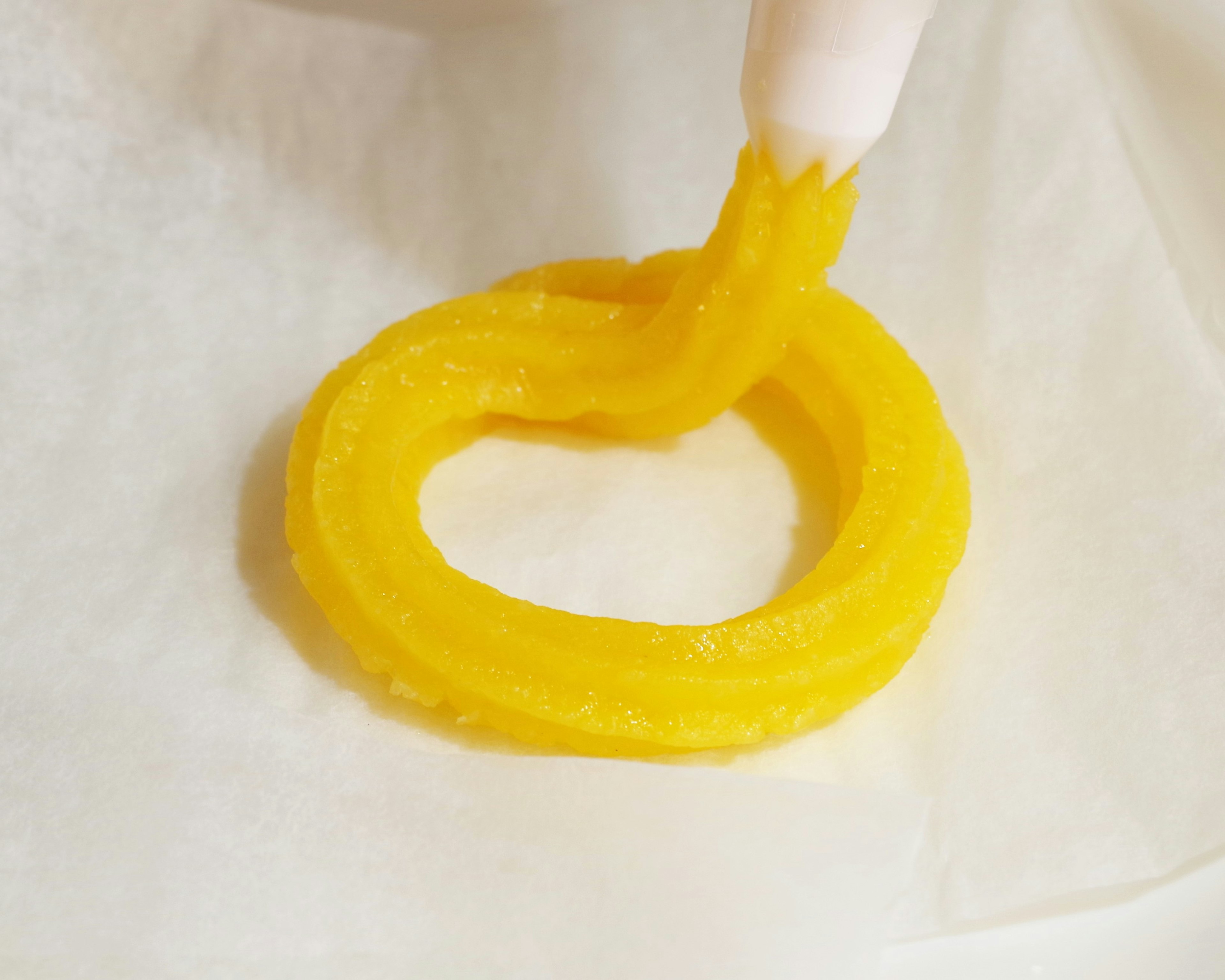 Yellow dessert ring being shaped on white parchment paper