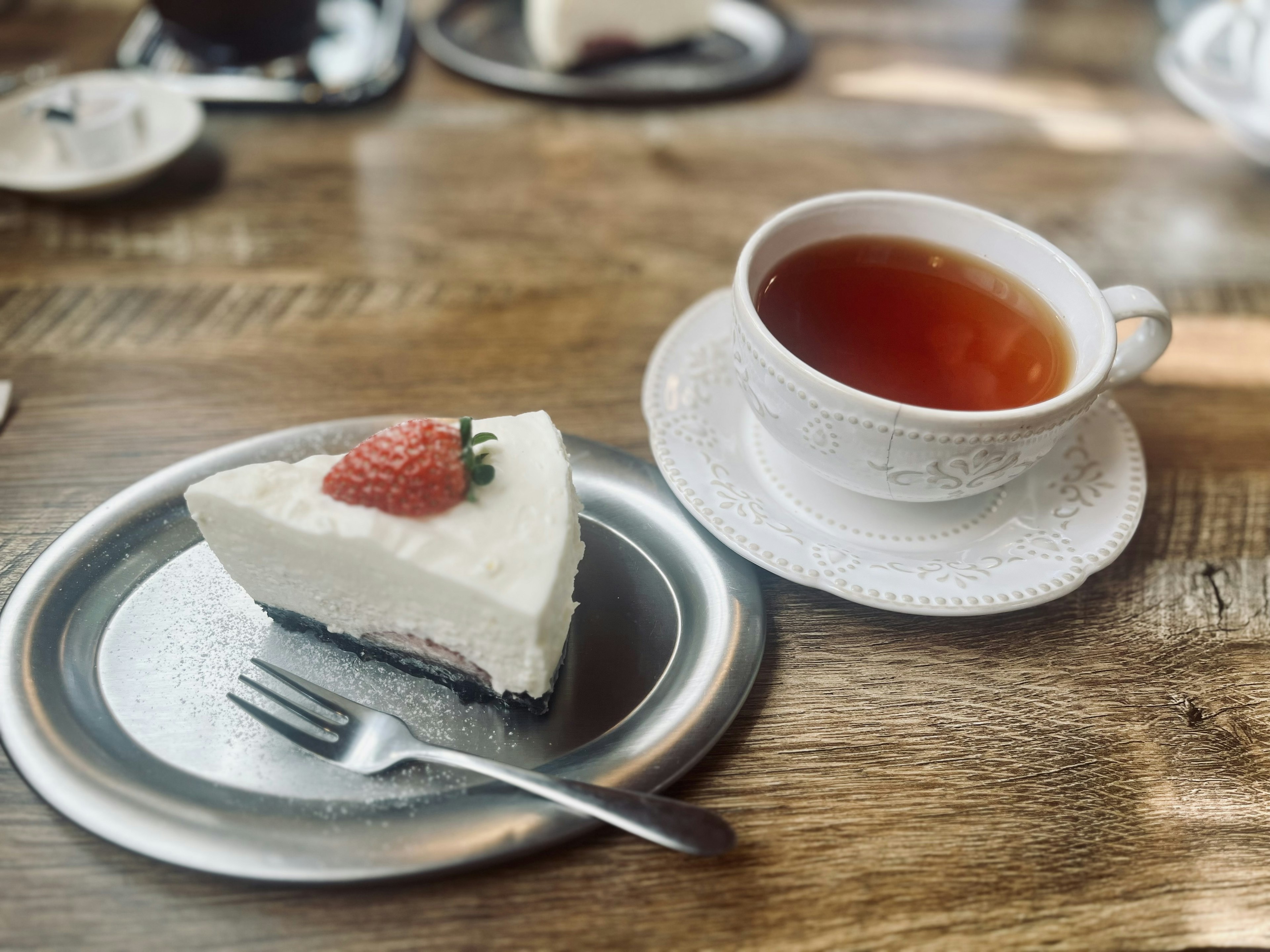 Slice of white cake topped with a strawberry next to a cup of tea