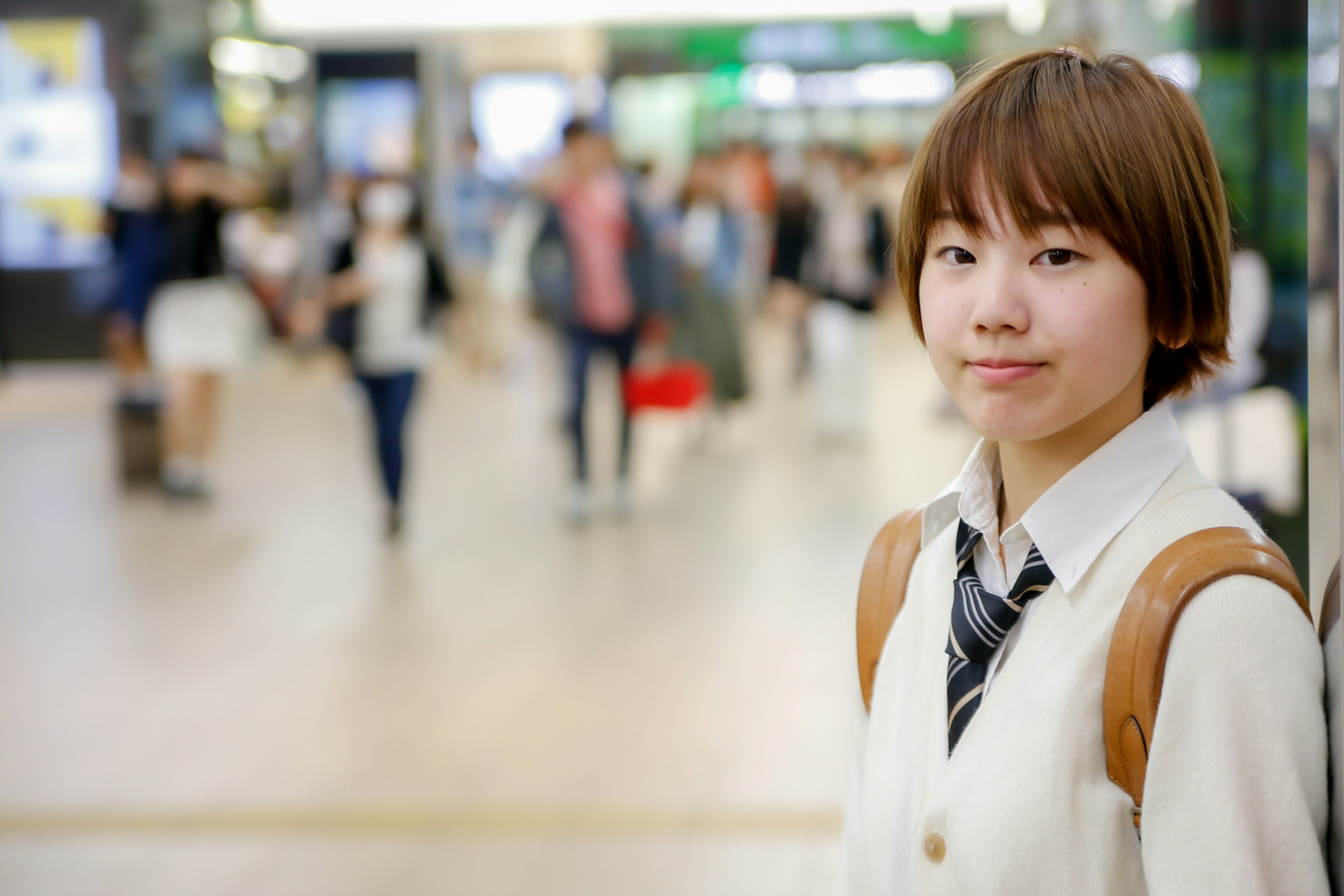 Portrait of a young woman smiling near a station with blurred people walking in the background