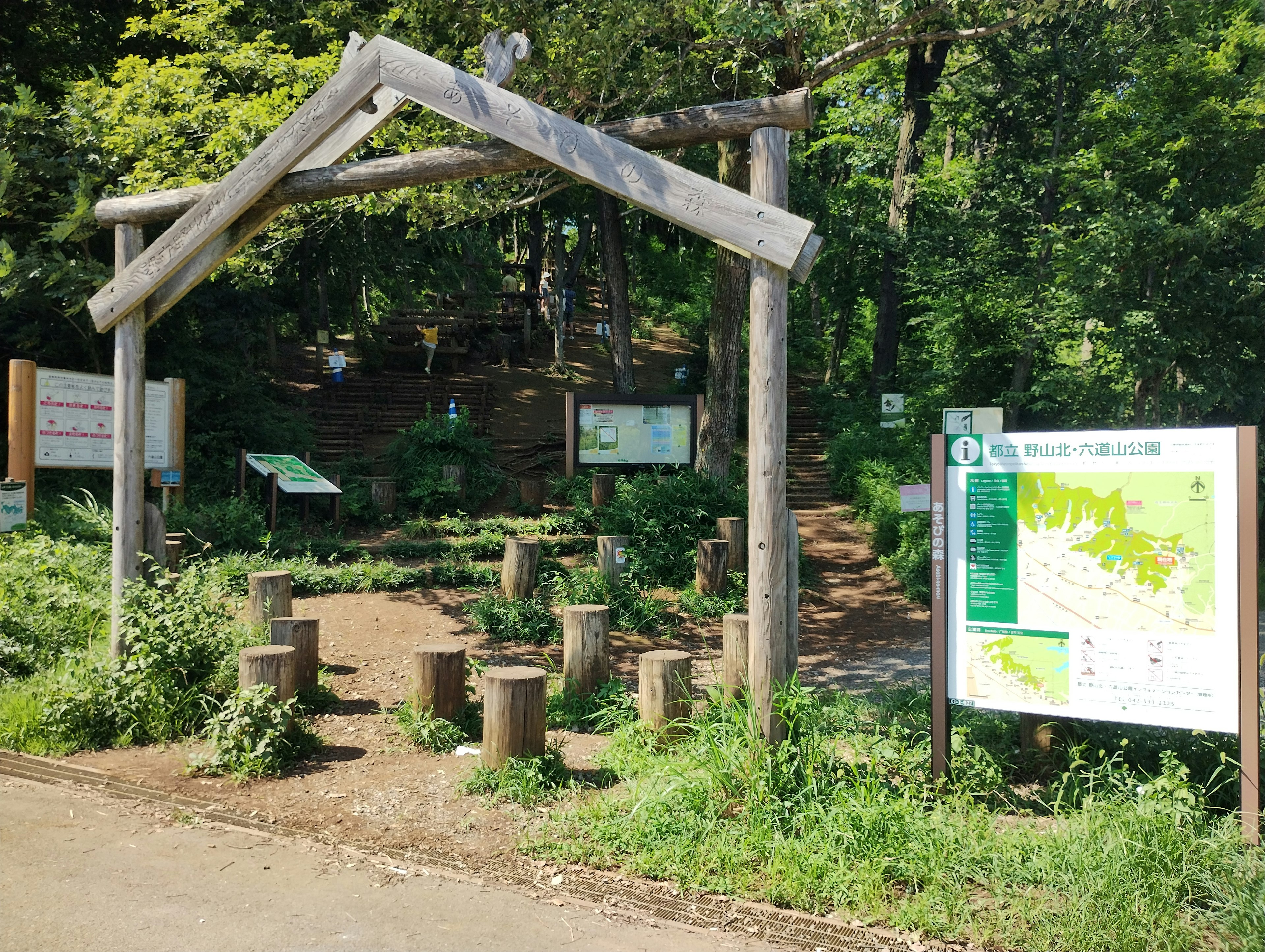 Entrada de arco de madera que conduce a un parque verde con paneles informativos