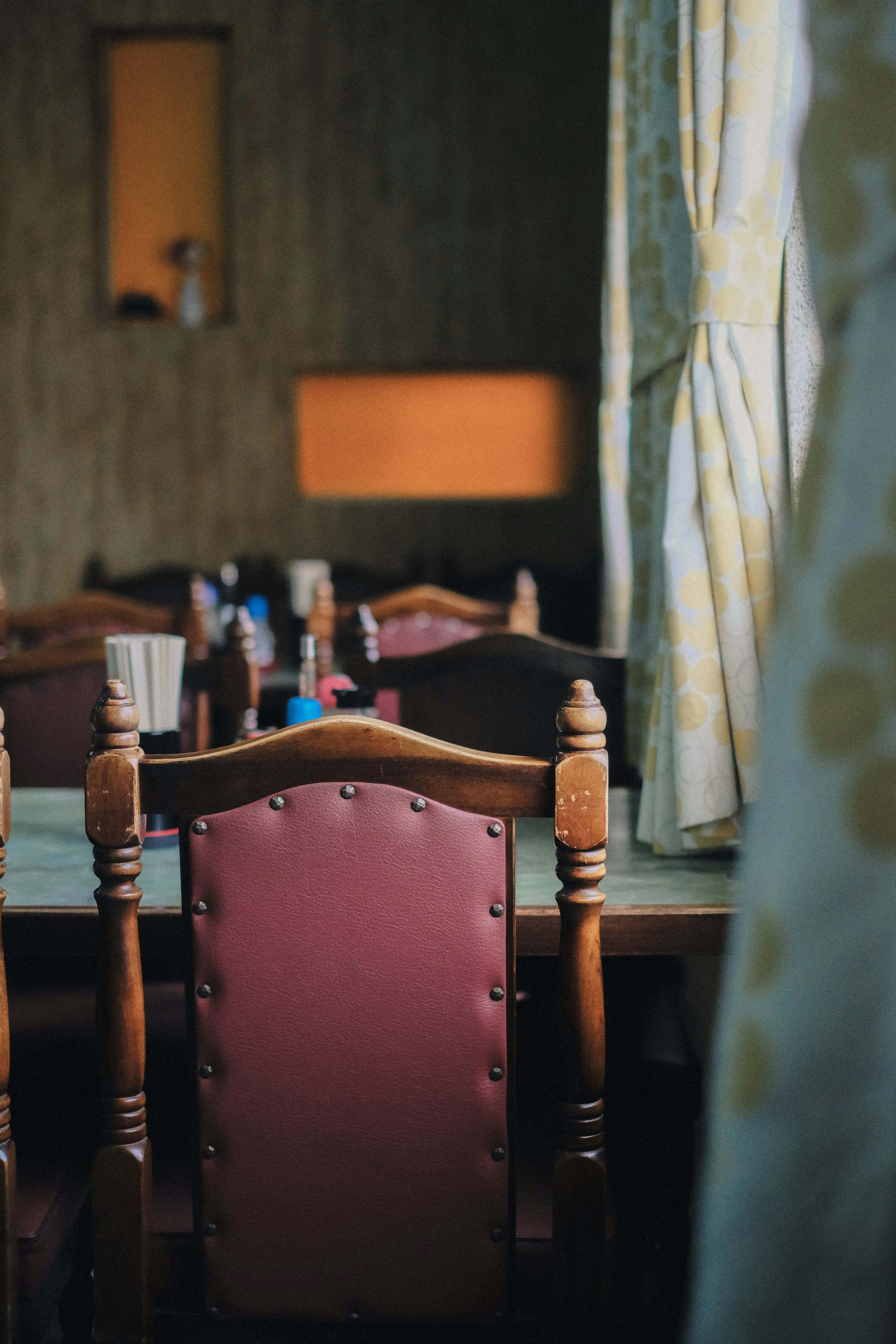 Una habitación acogedora con sillas dispuestas alrededor de una mesa luz suave que entra por la ventana y cortinas verdes que crean un ambiente cálido