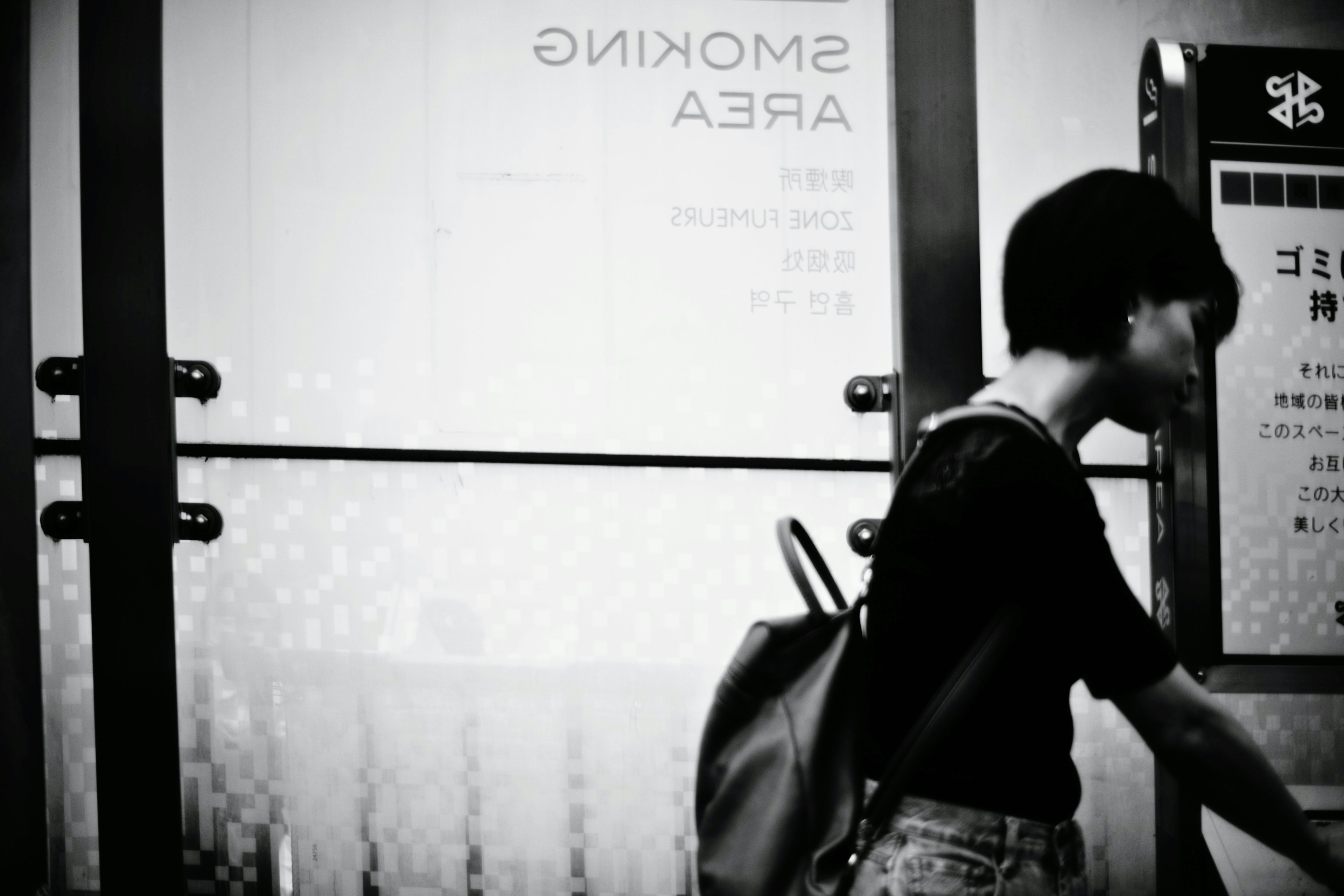 Black and white image of a woman passing by a smoking area sign