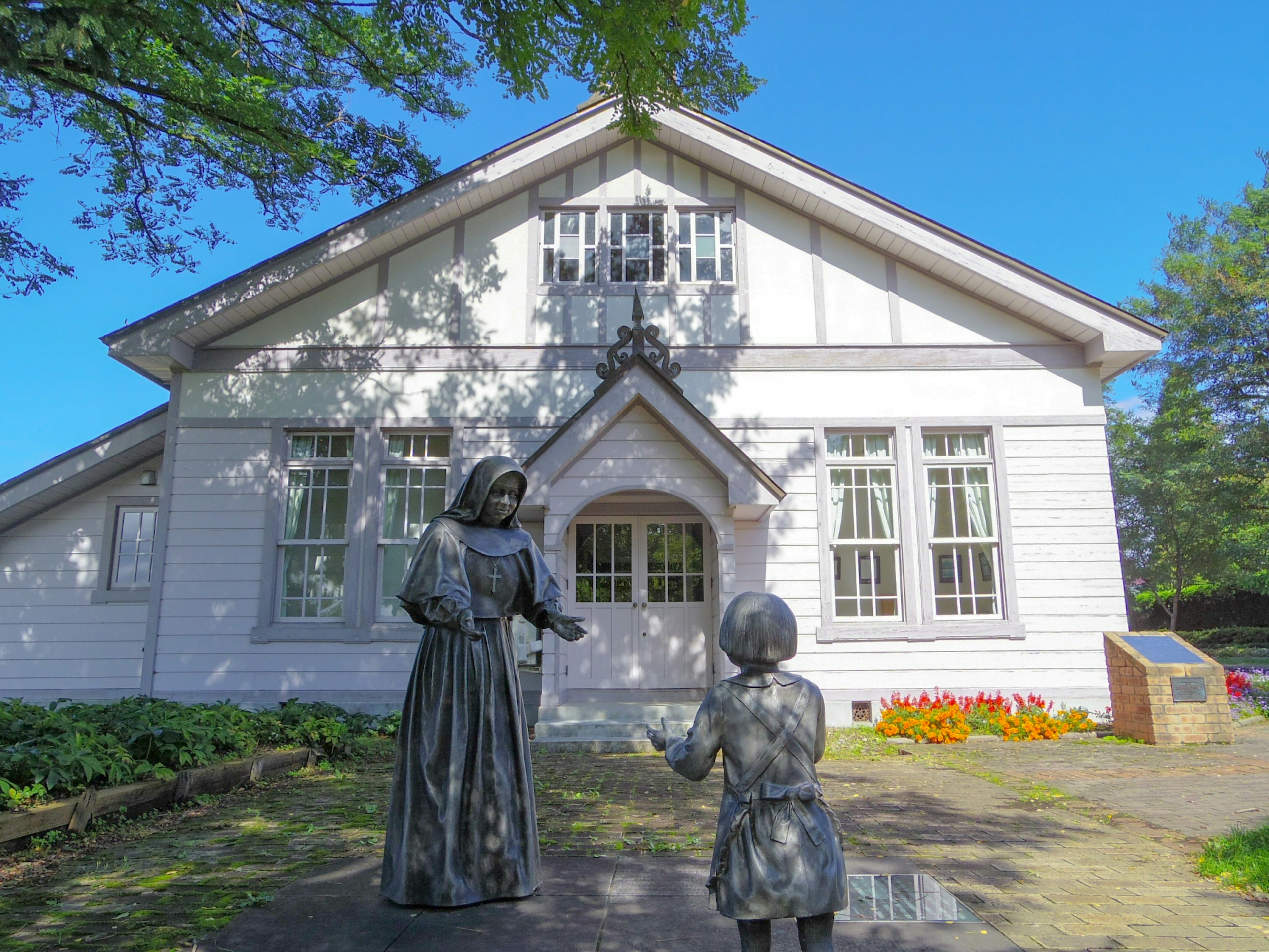 Deux statues en bronze devant un bâtiment blanc avec de grandes fenêtres et un jardin verdoyant