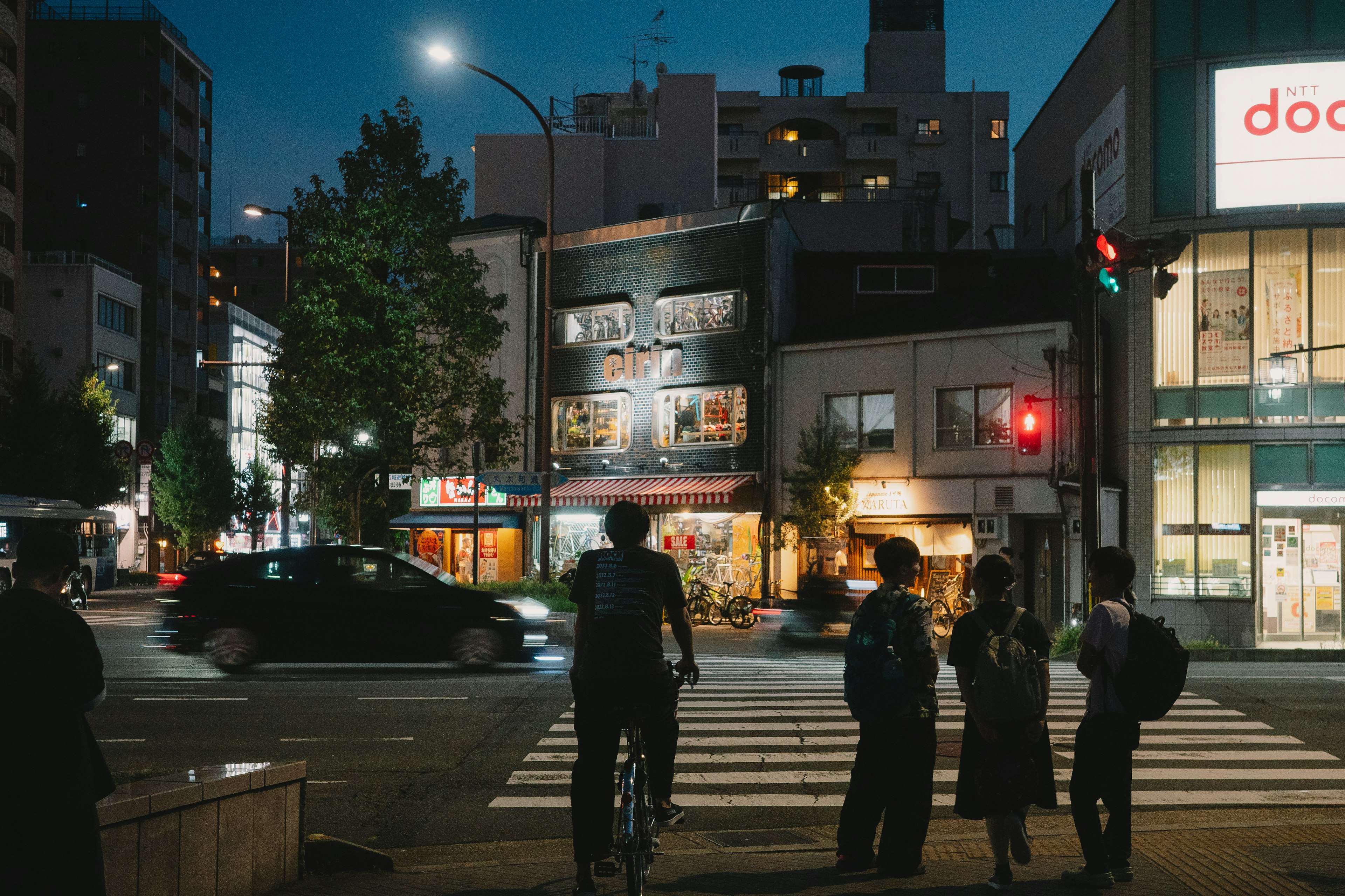 夜の街角で信号待ちをする人々と車