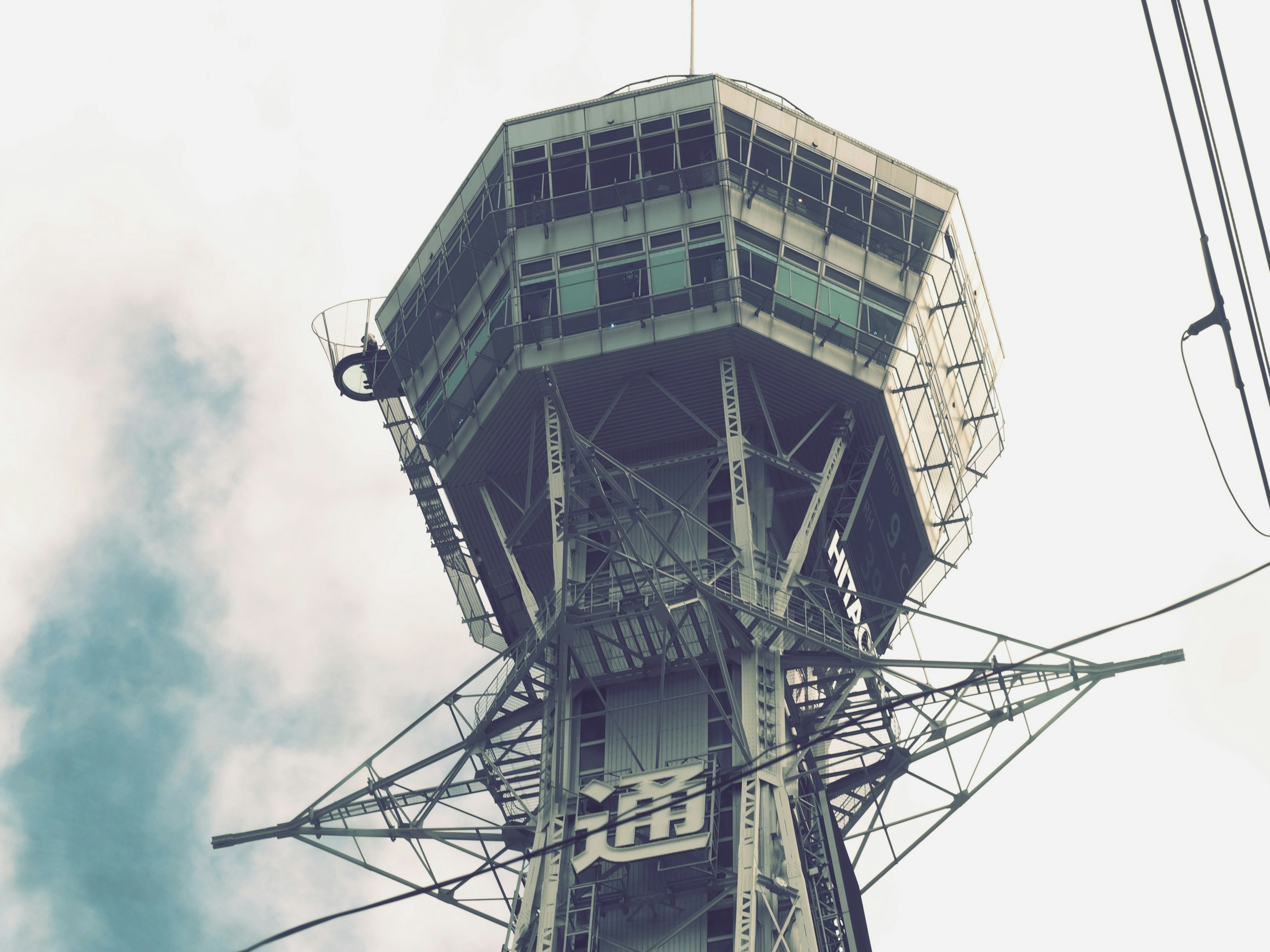 View of a tall tower structure with a control room and clouds in the background