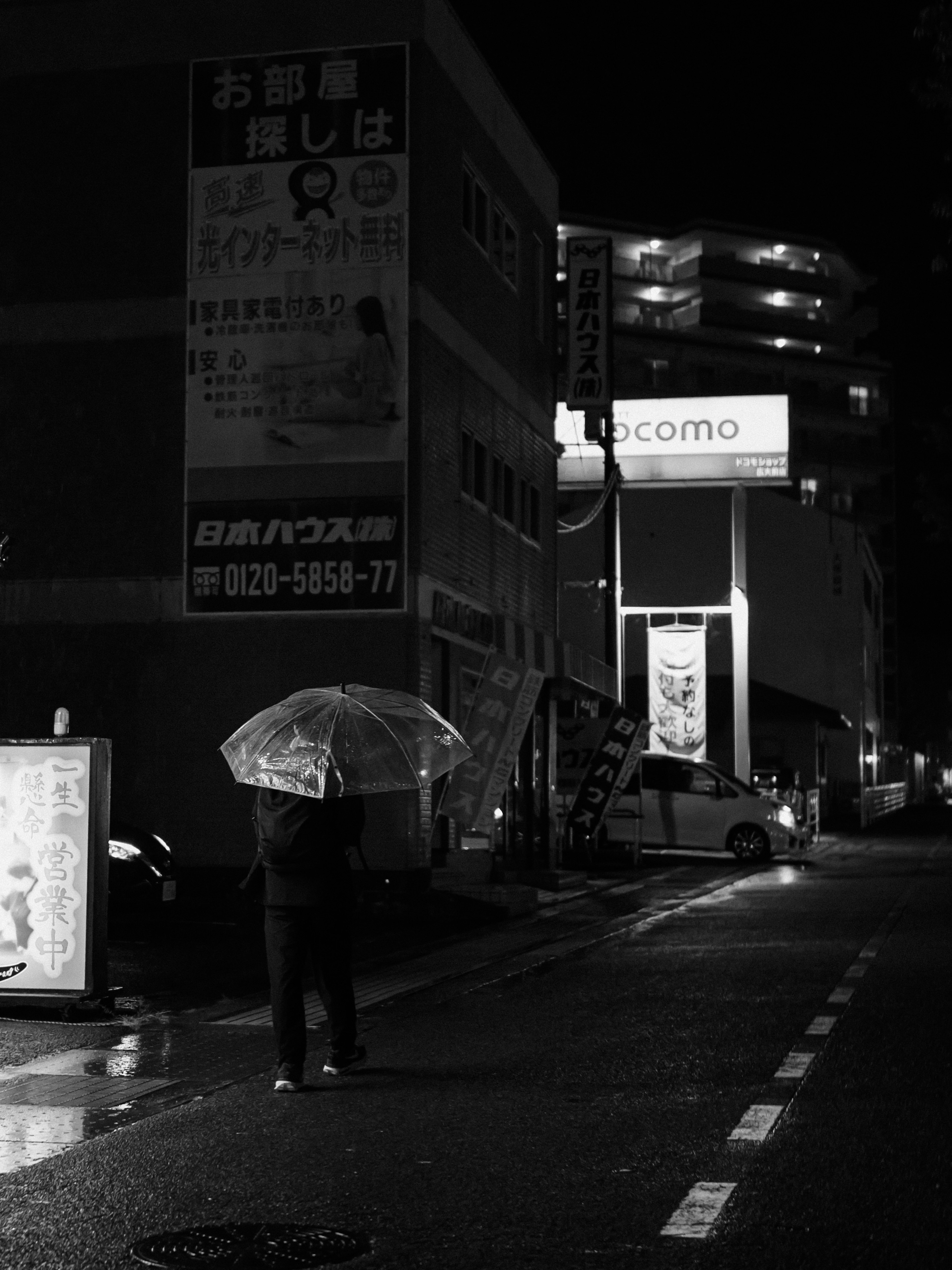 Eine Person mit einem Regenschirm unter einer Straßenlaterne in einer monochromen Stadtszene bei Nacht