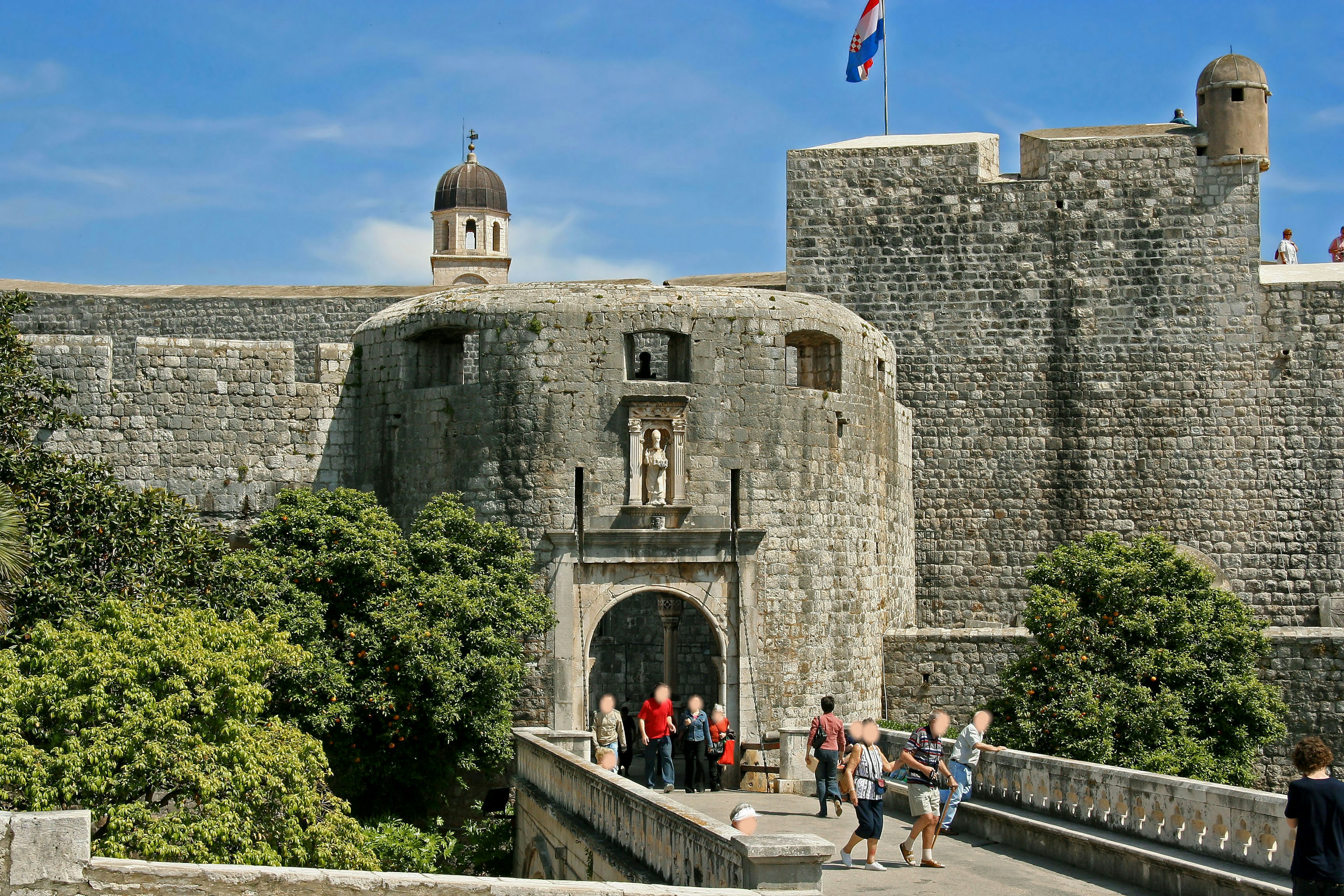 Puerta de castillo de piedra rodeada de vegetación y visitantes