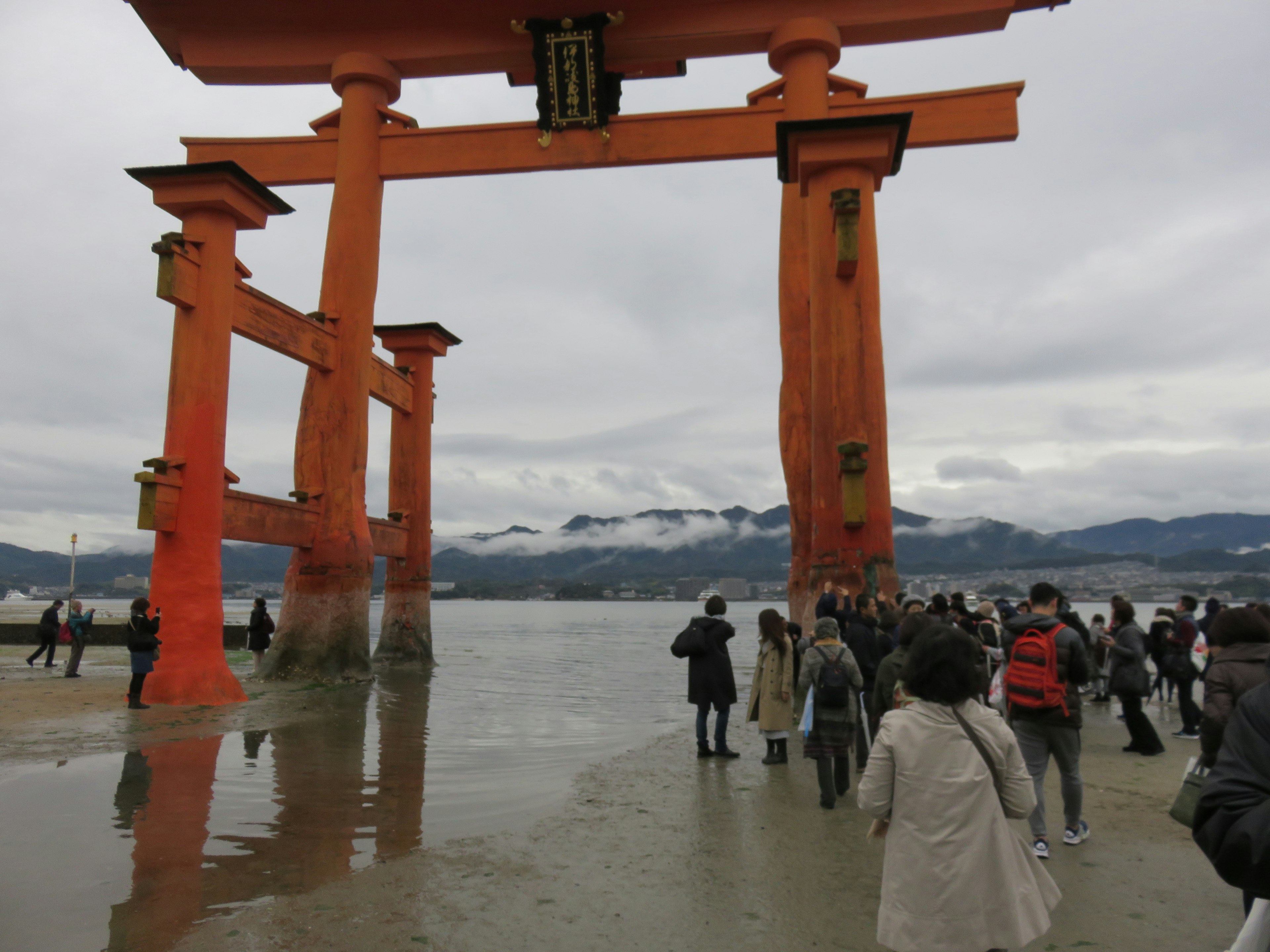 A view of the orange torii gate of Itsukushima Shrine with tourists in the foreground