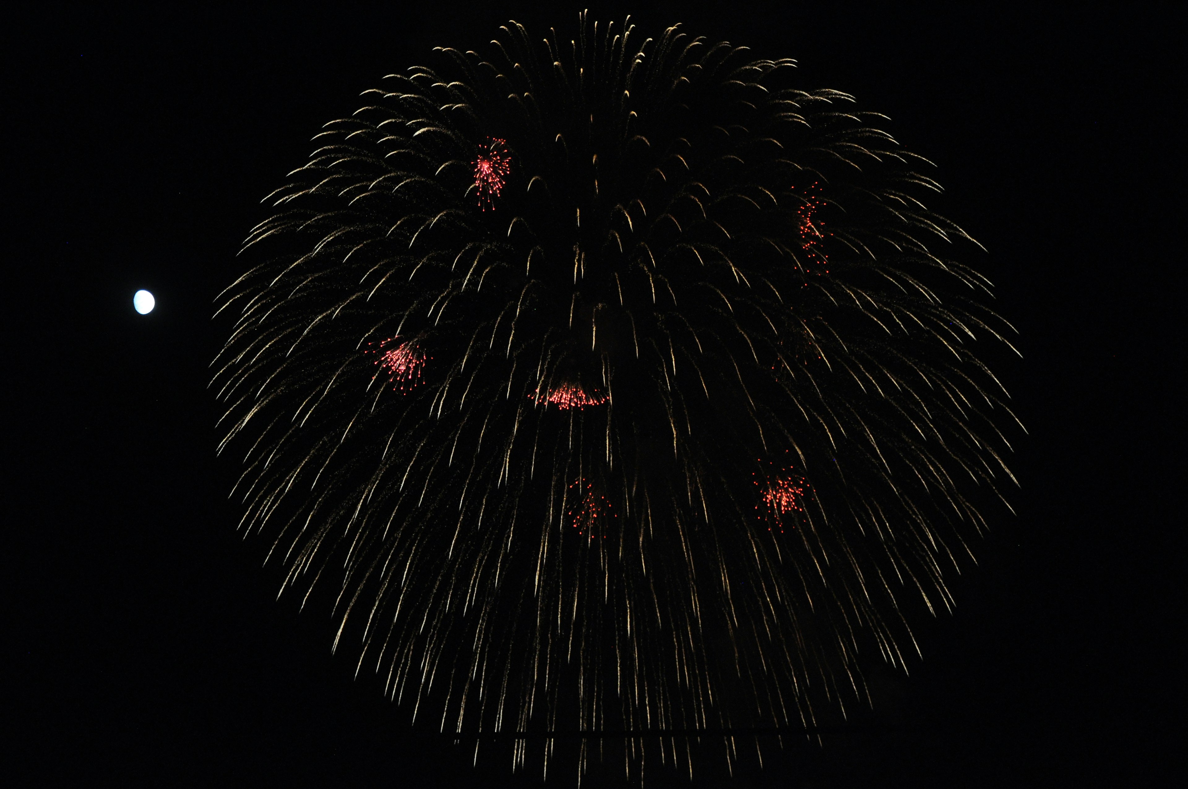 Sphärische Explosion von Feuerwerk vor schwarzem Hintergrund mit einem kleinen Mond