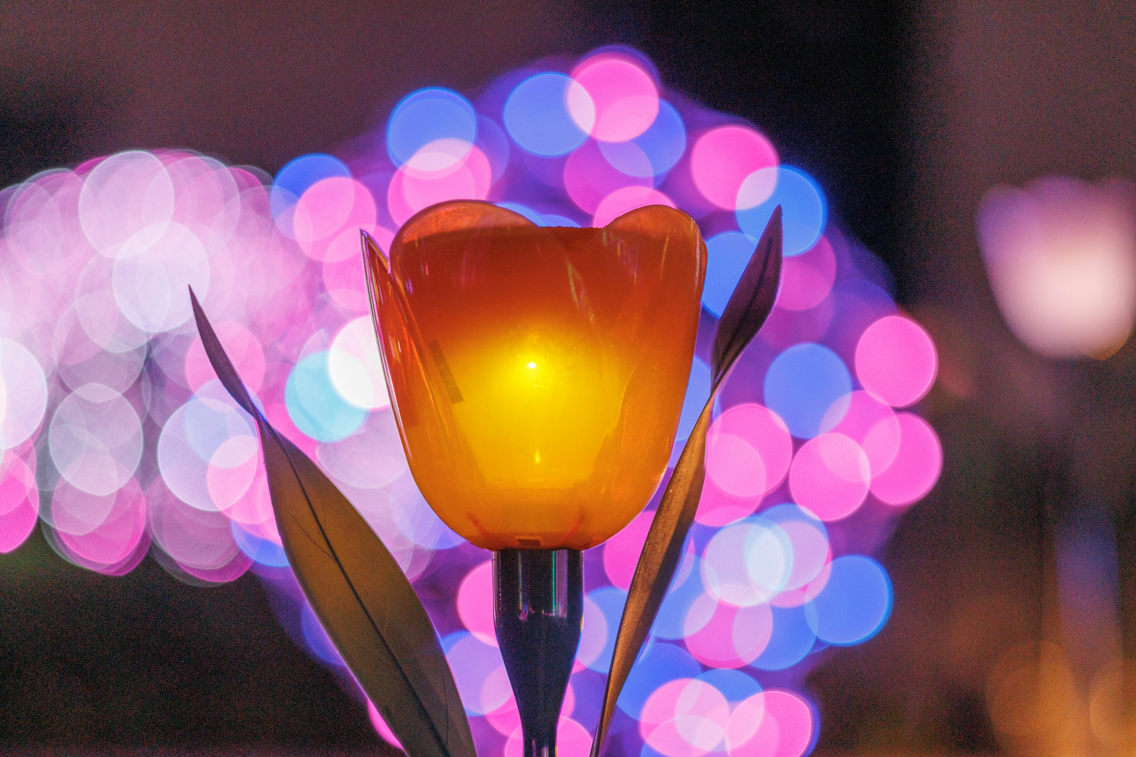 Lampu berbentuk tulip oranye di latar depan dengan cahaya bokeh berwarna-warni di latar belakang