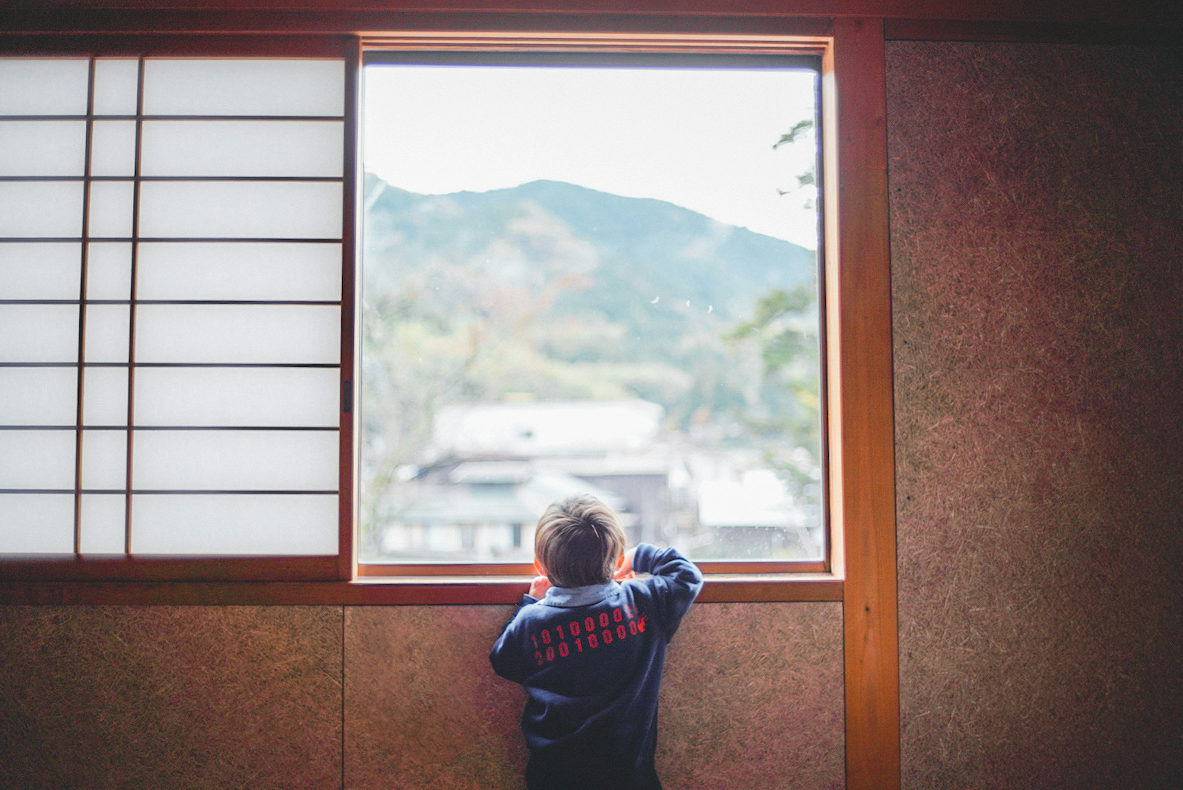 窓の外を見つめる子供の姿と山の風景