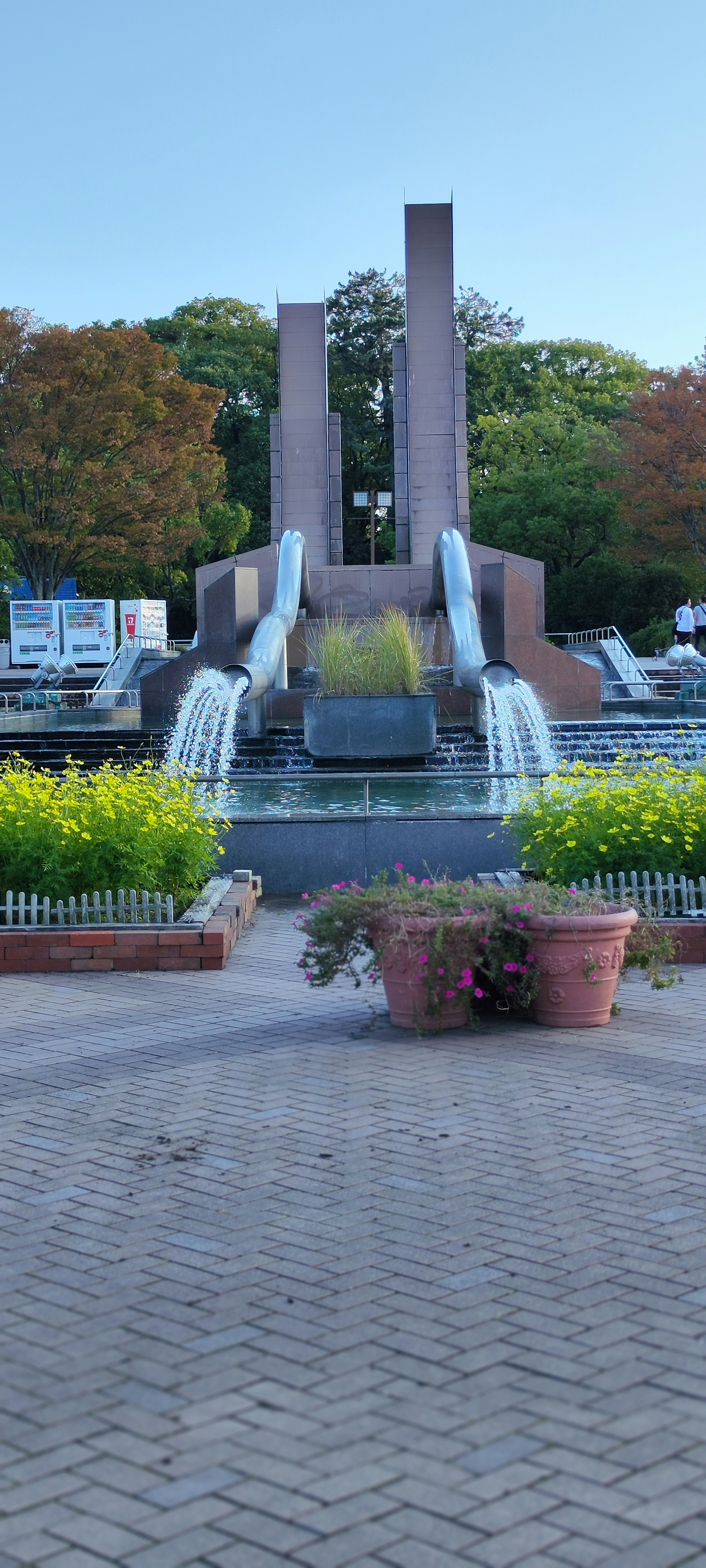 Fountain at the center of a park surrounded by greenery and flower pots