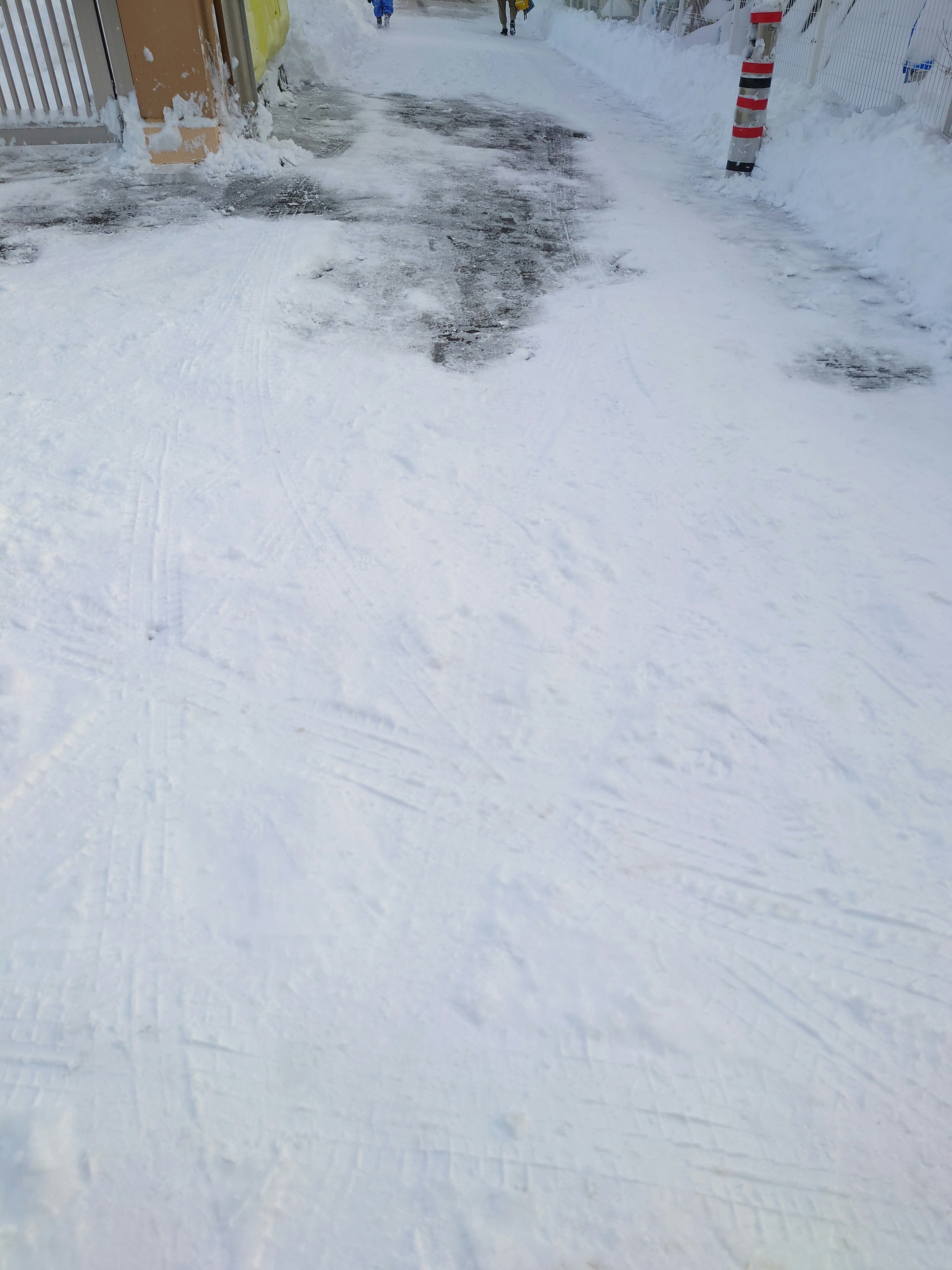 Schneebedeckter Gehweg mit sichtbarem gelben Gebäude und Verkehrsschild