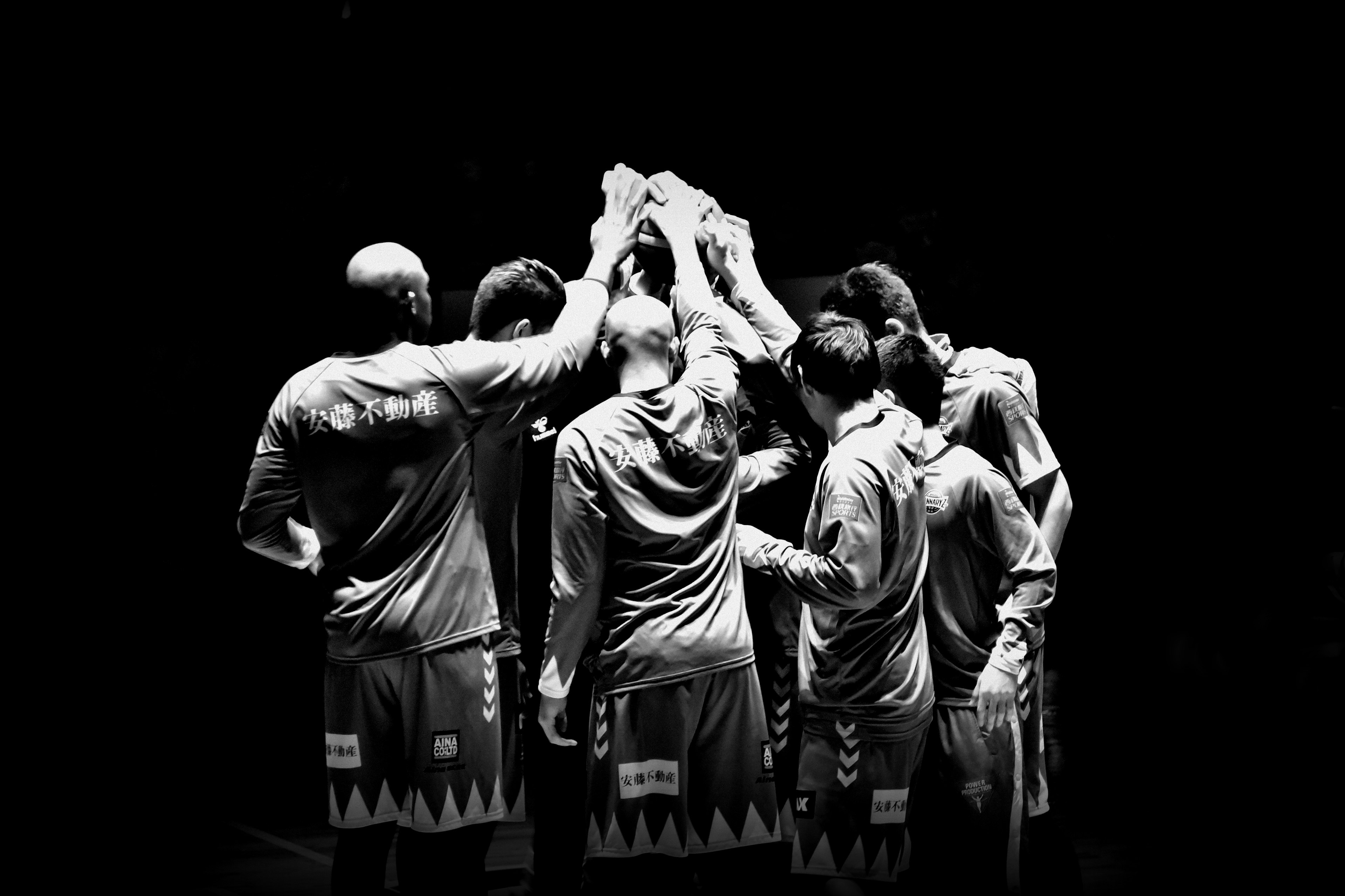 Photo en noir et blanc d'une équipe de basketball se regroupant avec les mains levées