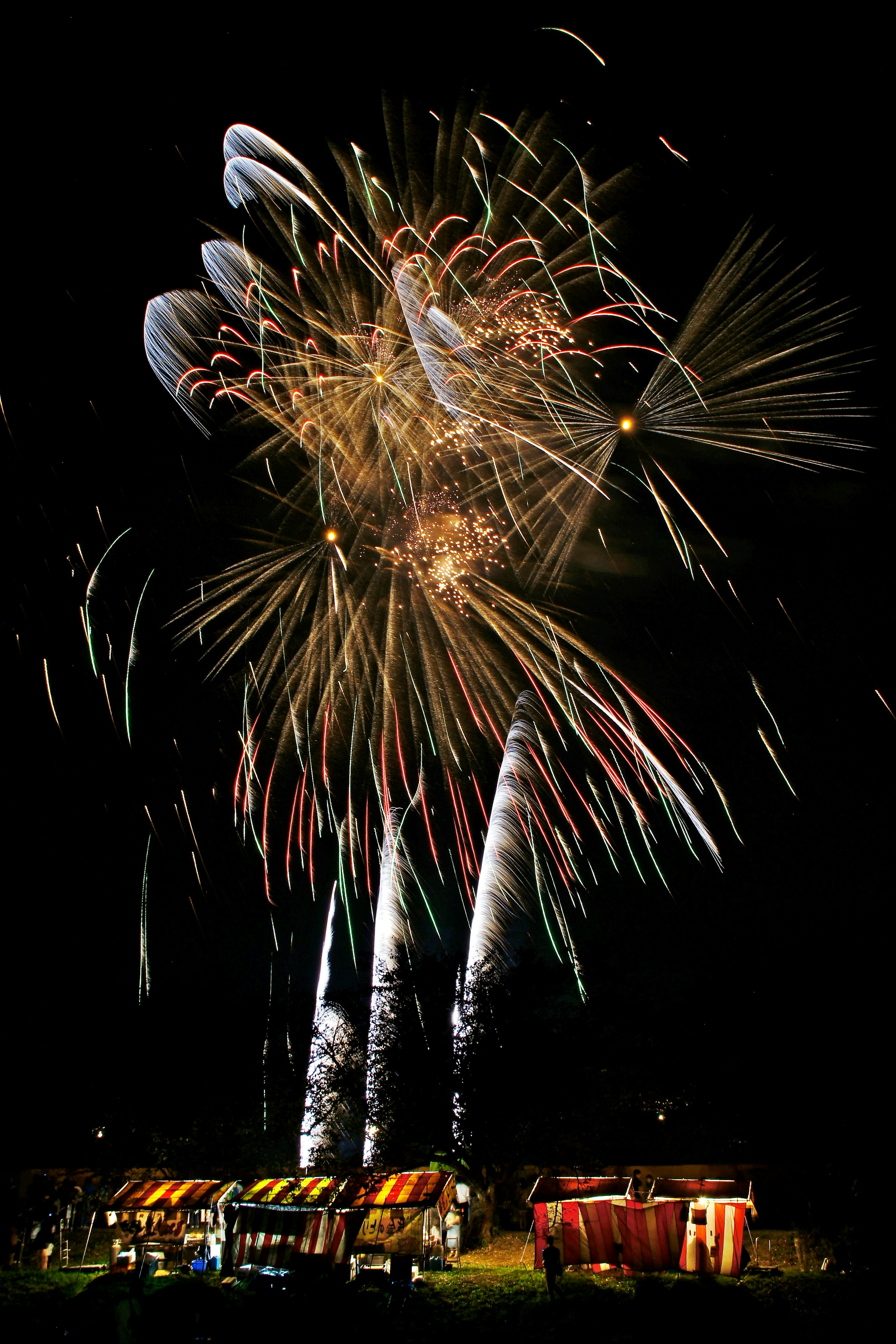 Fuochi d'artificio colorati che esplodono nel cielo notturno con bancarelle illuminate in primo piano