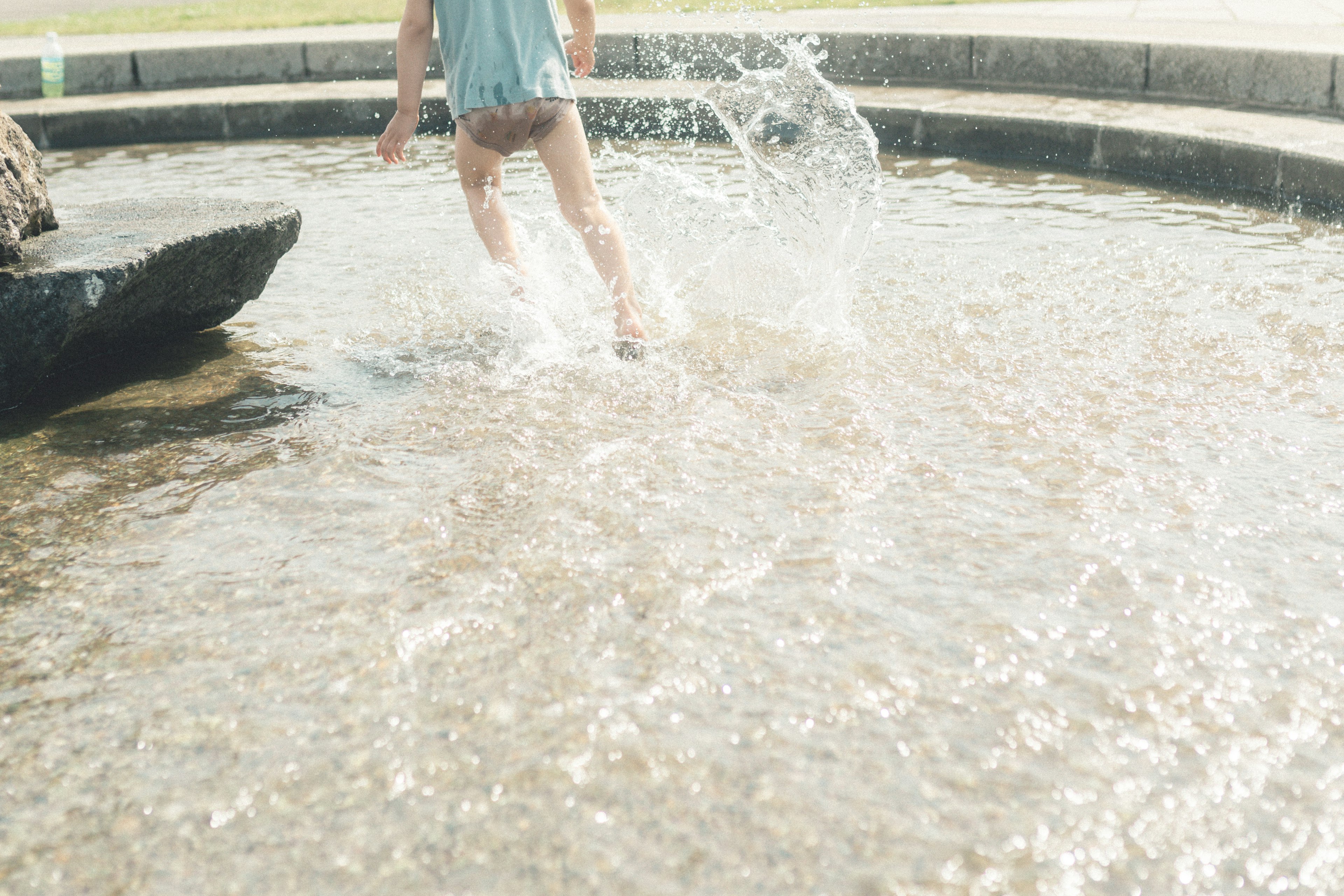 Enfant éclaboussant dans l'eau peu profonde avec bord en pierre