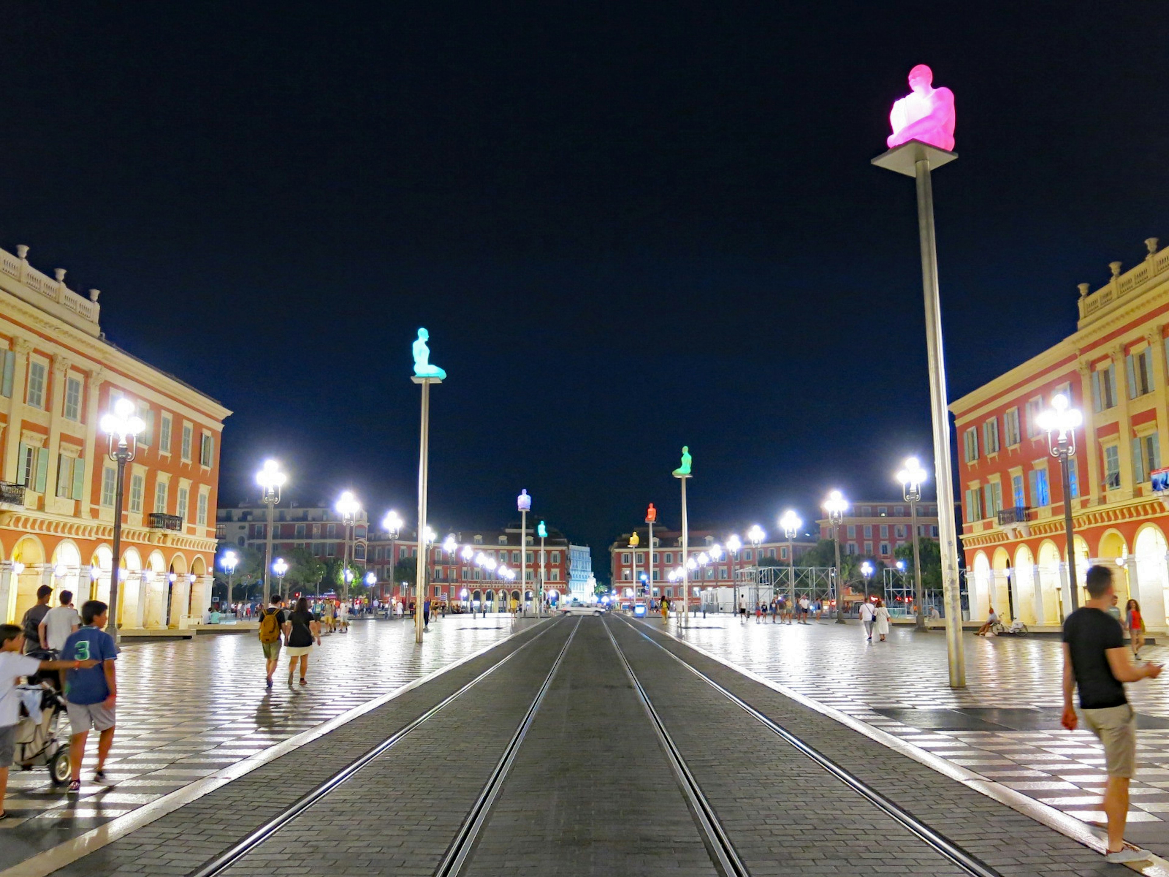 Sculture colorate che illuminano la strada di notte con persone che camminano