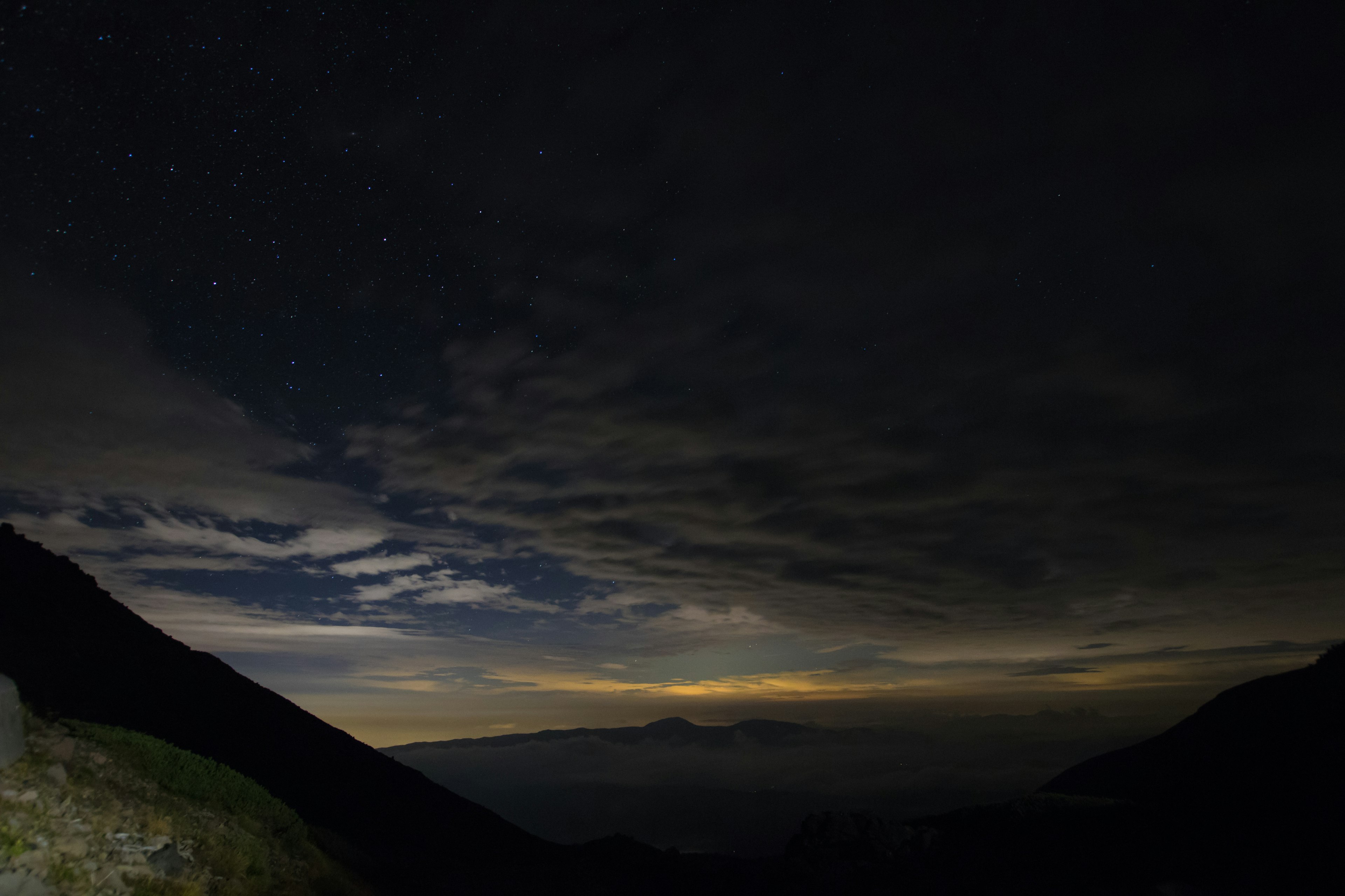 Paisaje montañoso bajo un cielo estrellado con nubes flotantes