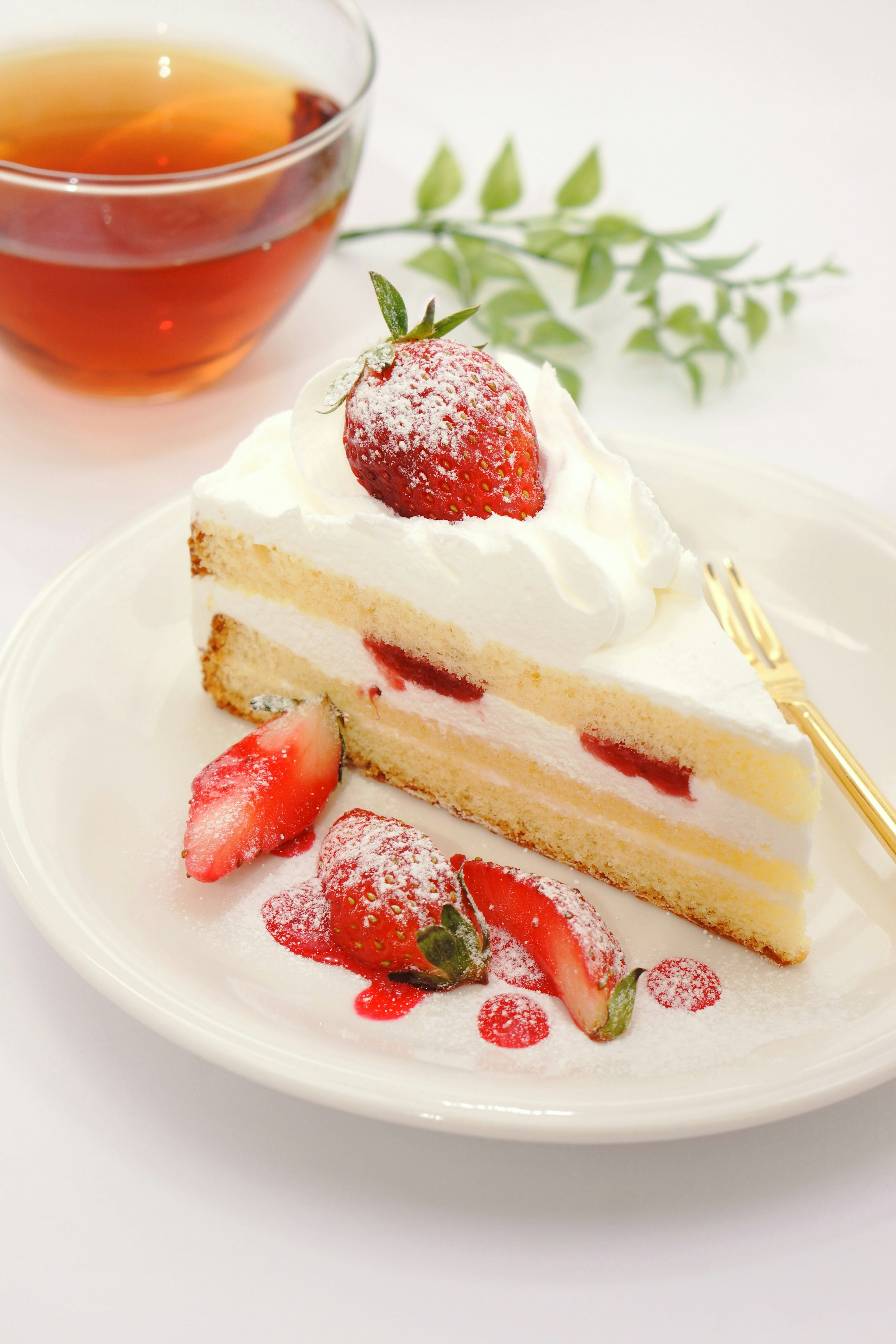 Fetta di torta alle fragole con panna montata e una tazza di tè su un piatto bianco