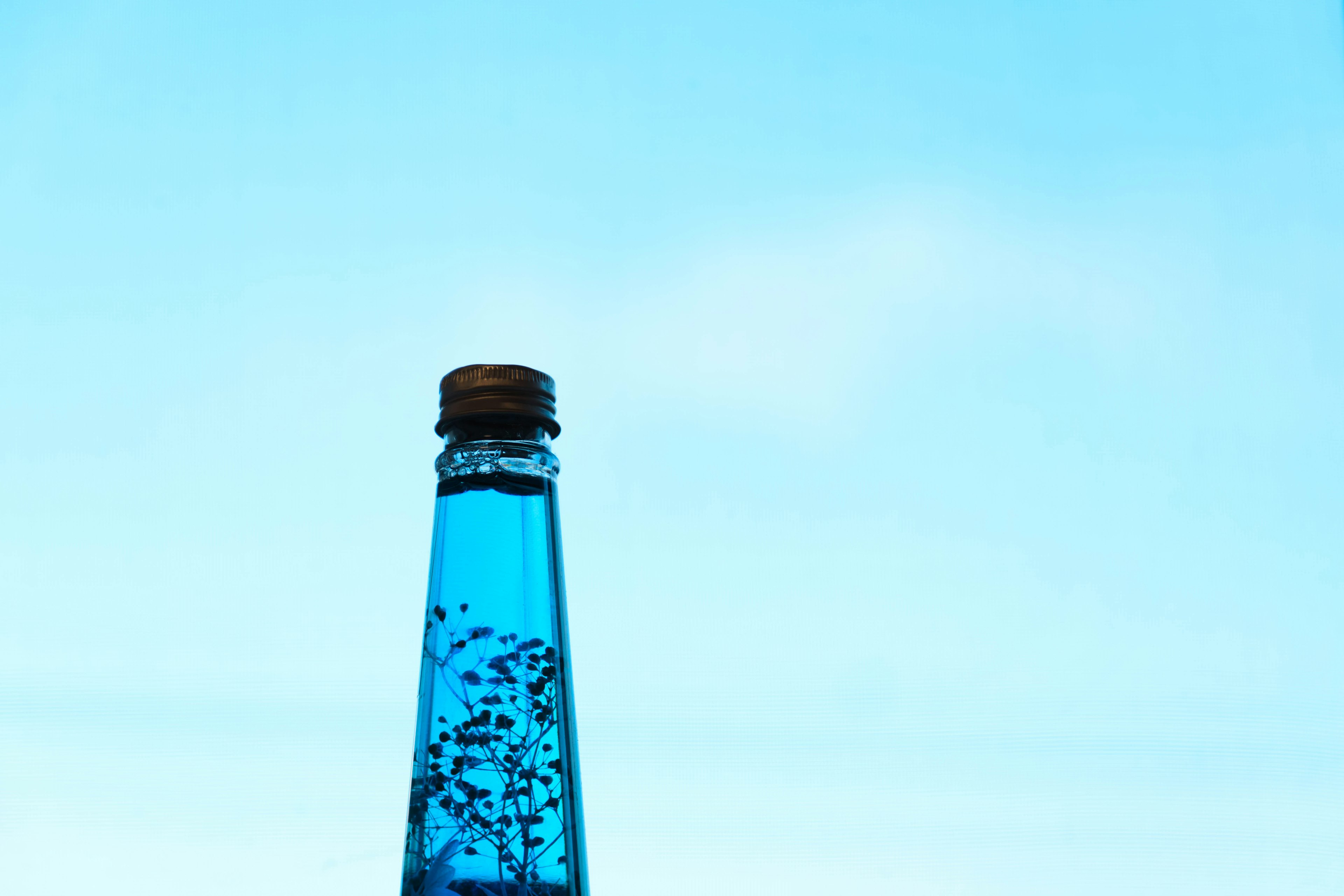 Botella azul con líquido transparente y burbujas contra un cielo claro