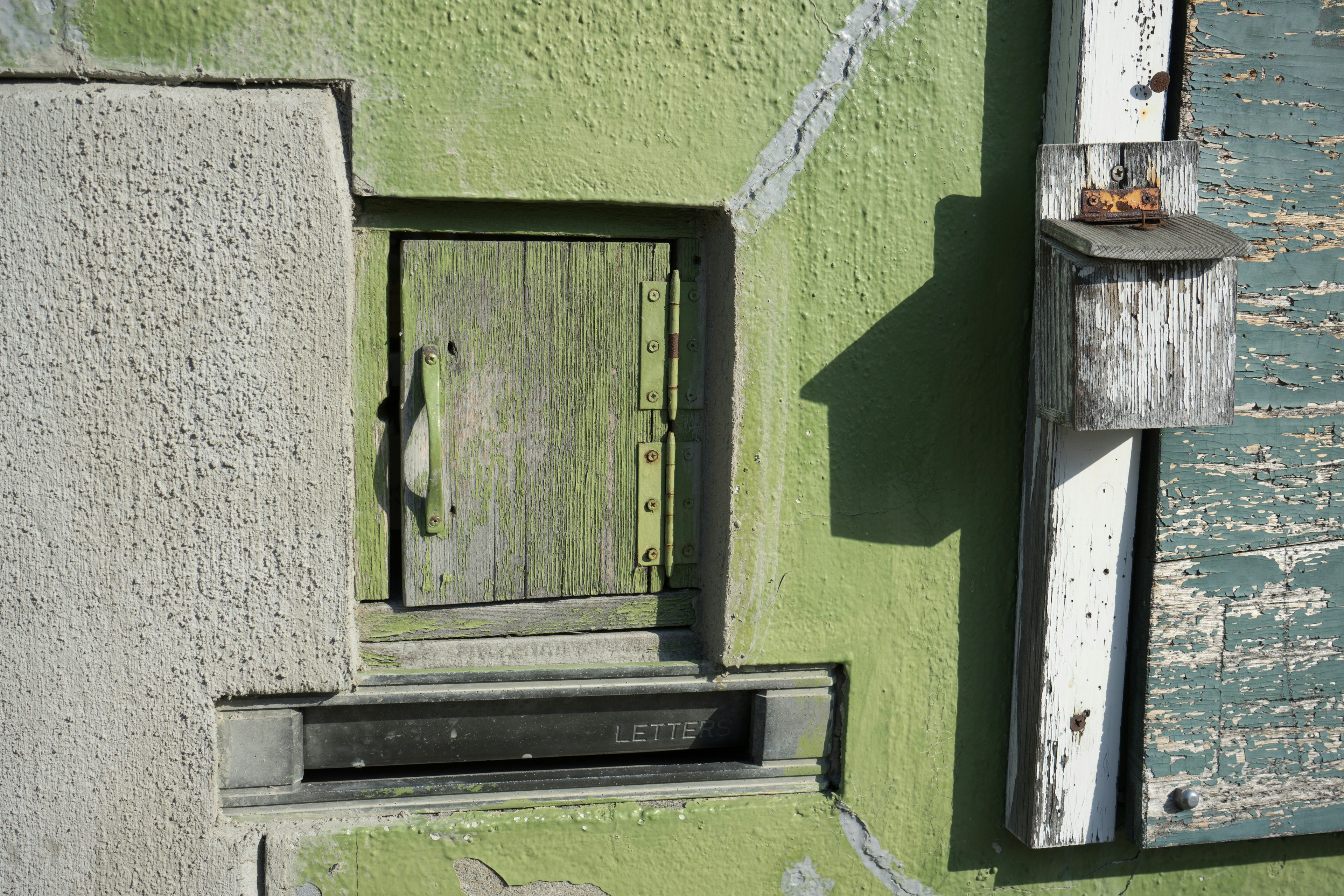 Imagen de una pequeña puerta de madera y un buzón en una pared verde