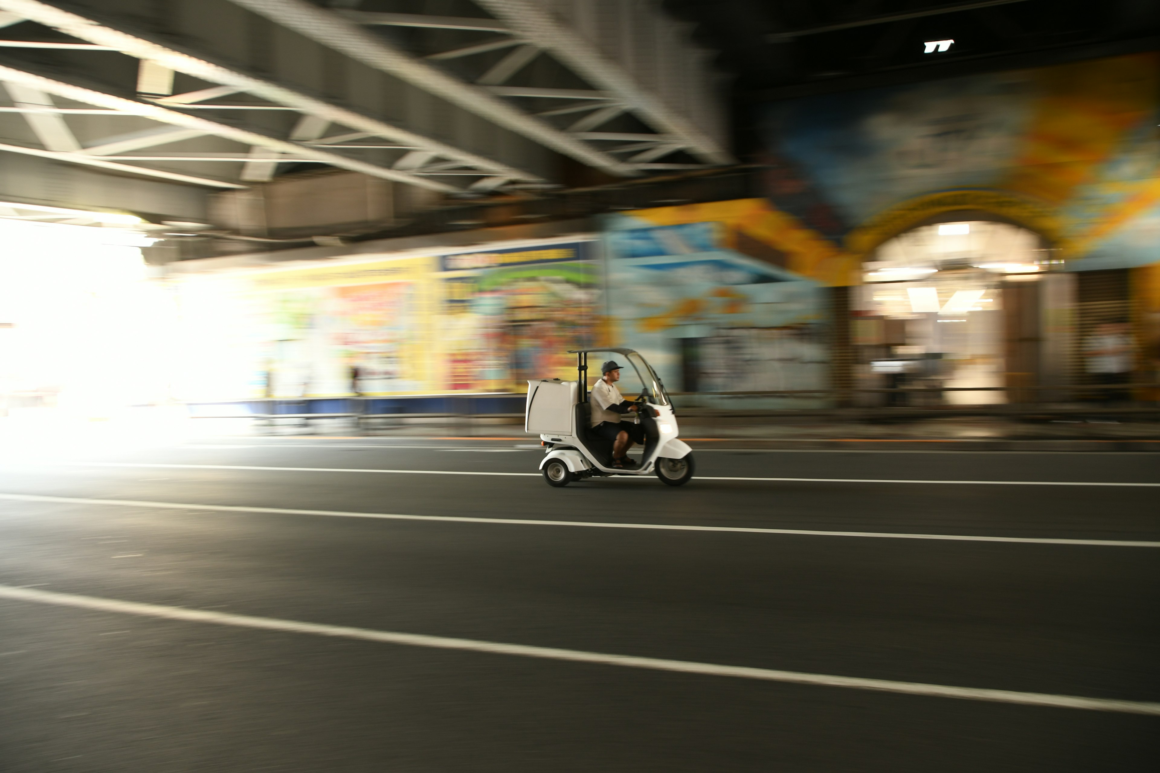 A white tricycle in motion under an urban setting with colorful murals