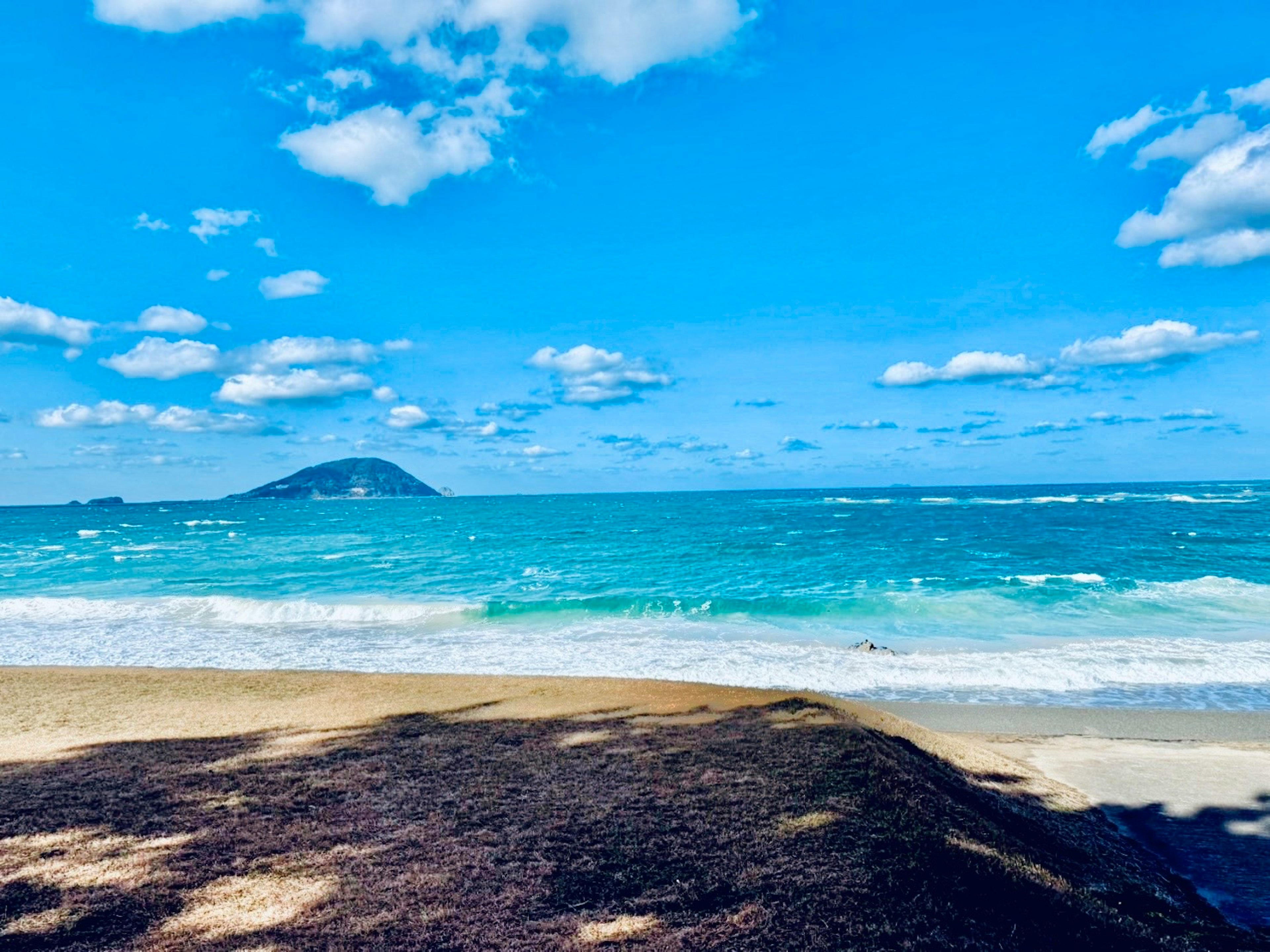 青い海と空の景色に小島が見えるビーチ