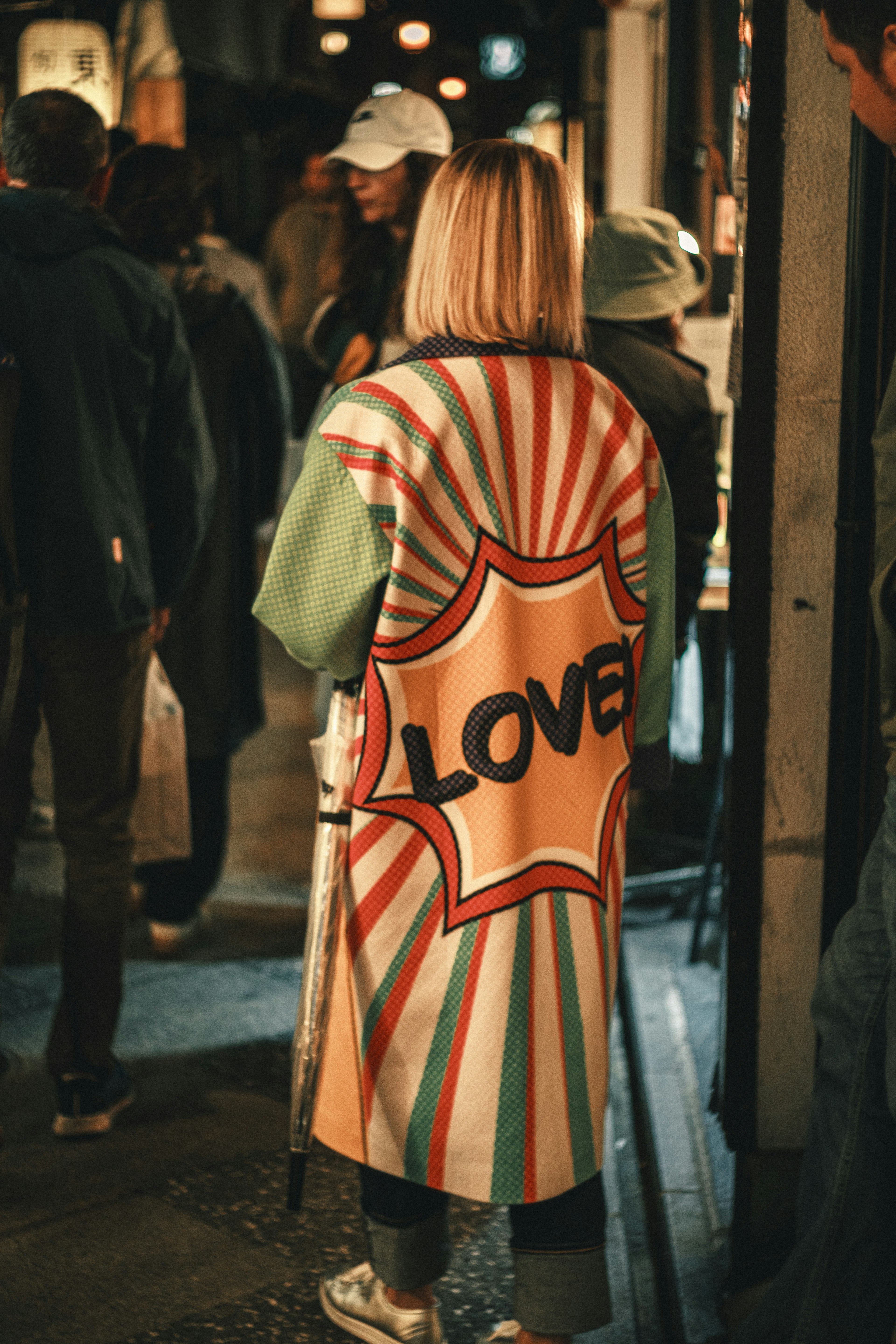 A woman wearing a colorful coat with a 'LOVE' graphic in a busy street scene