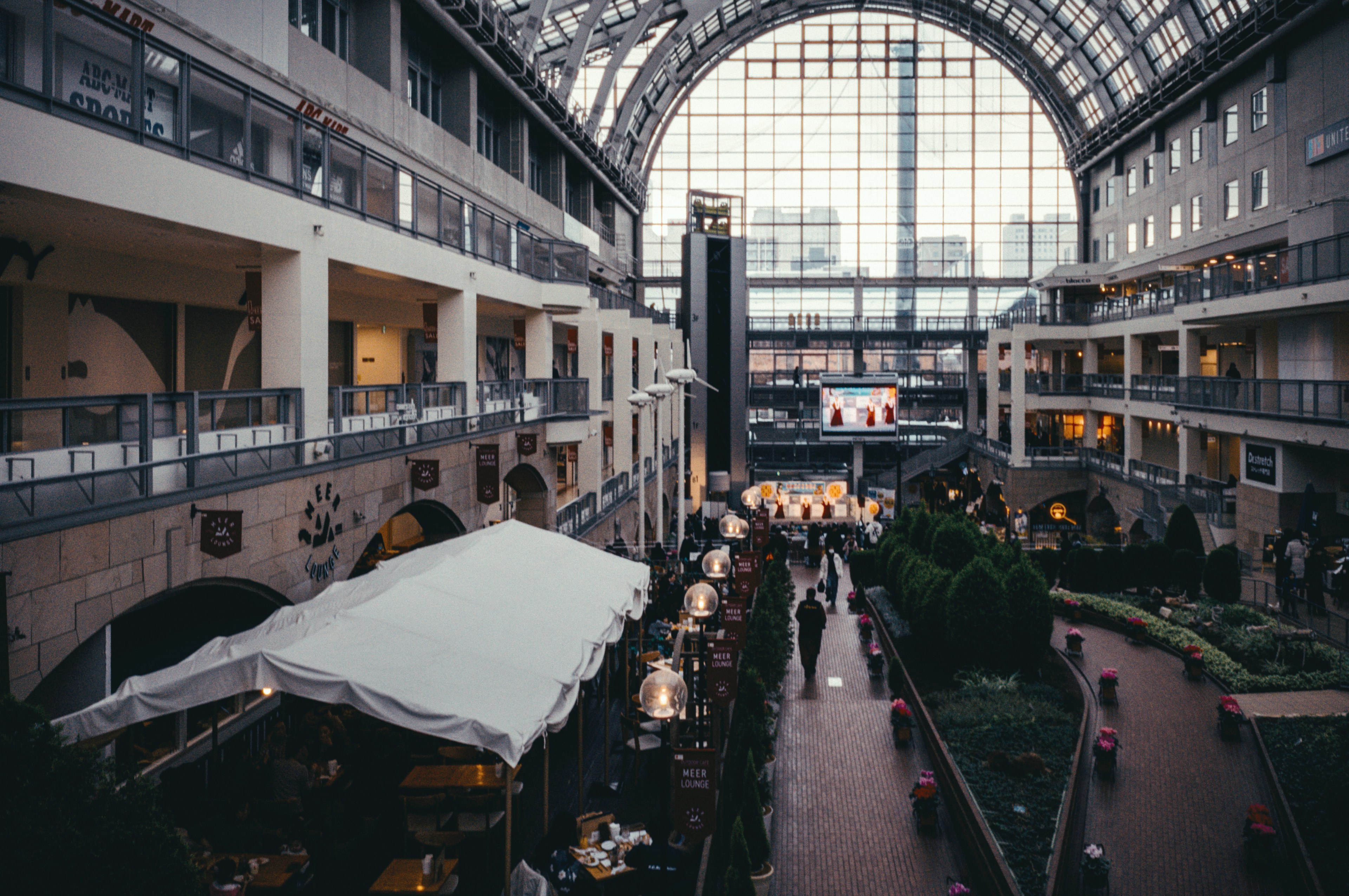 Interno spazioso di un centro commerciale con grande soffitto di vetro luce solare che entra vari negozi e persone che camminano