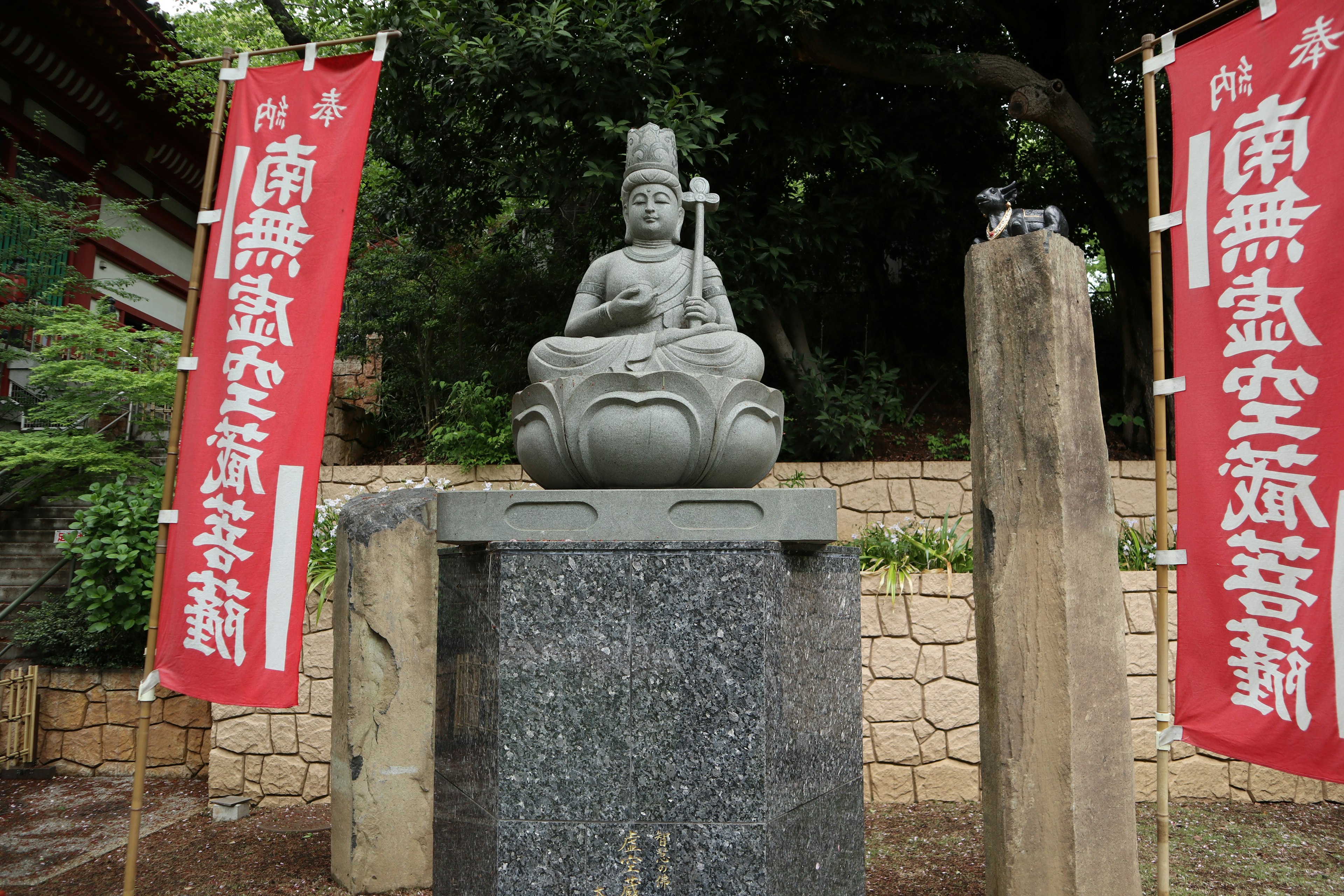 Statue en pierre d'une divinité entourée de verdure avec des bannières rouges de chaque côté