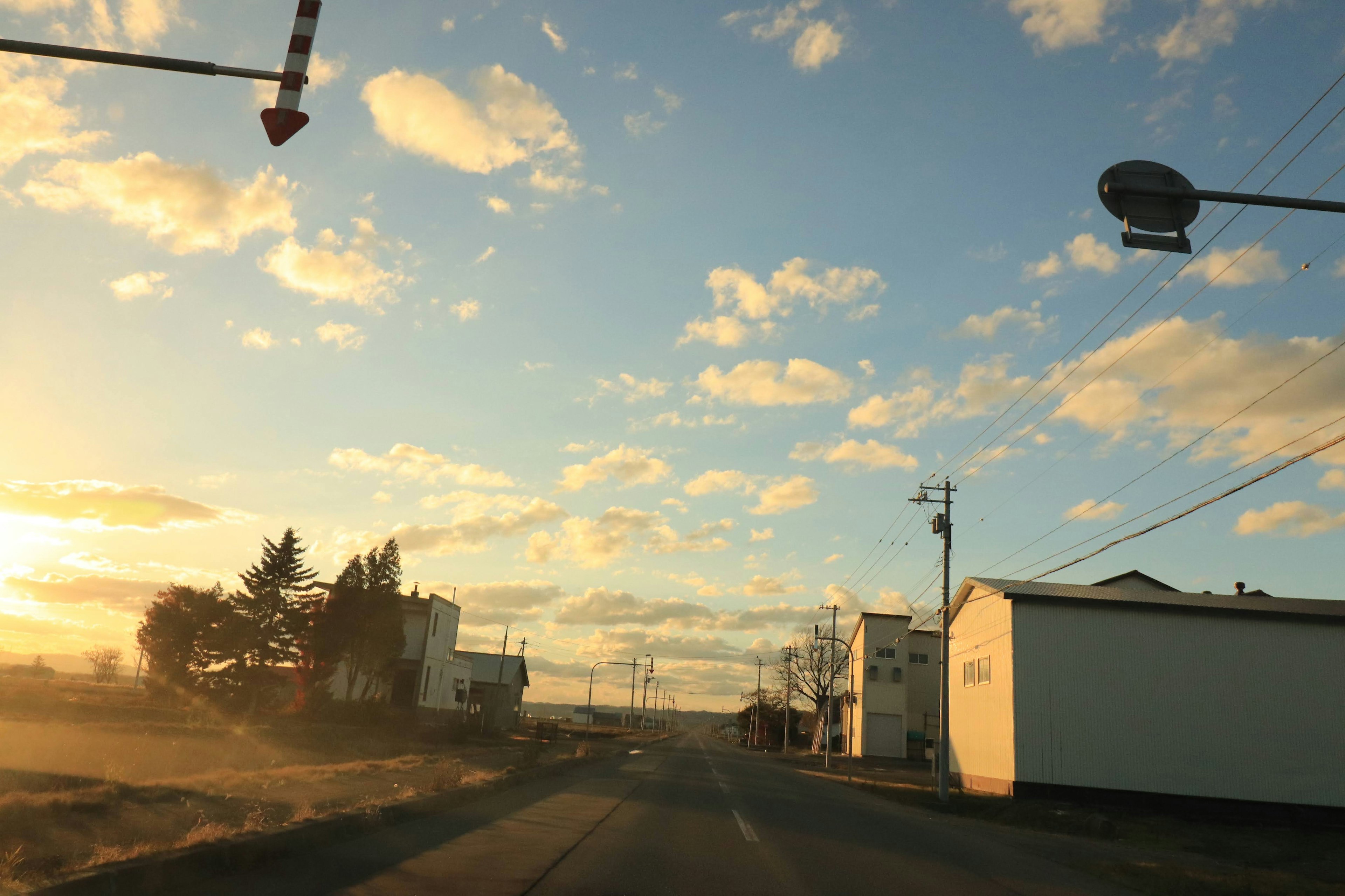 Road and buildings under a sunset with scattered clouds