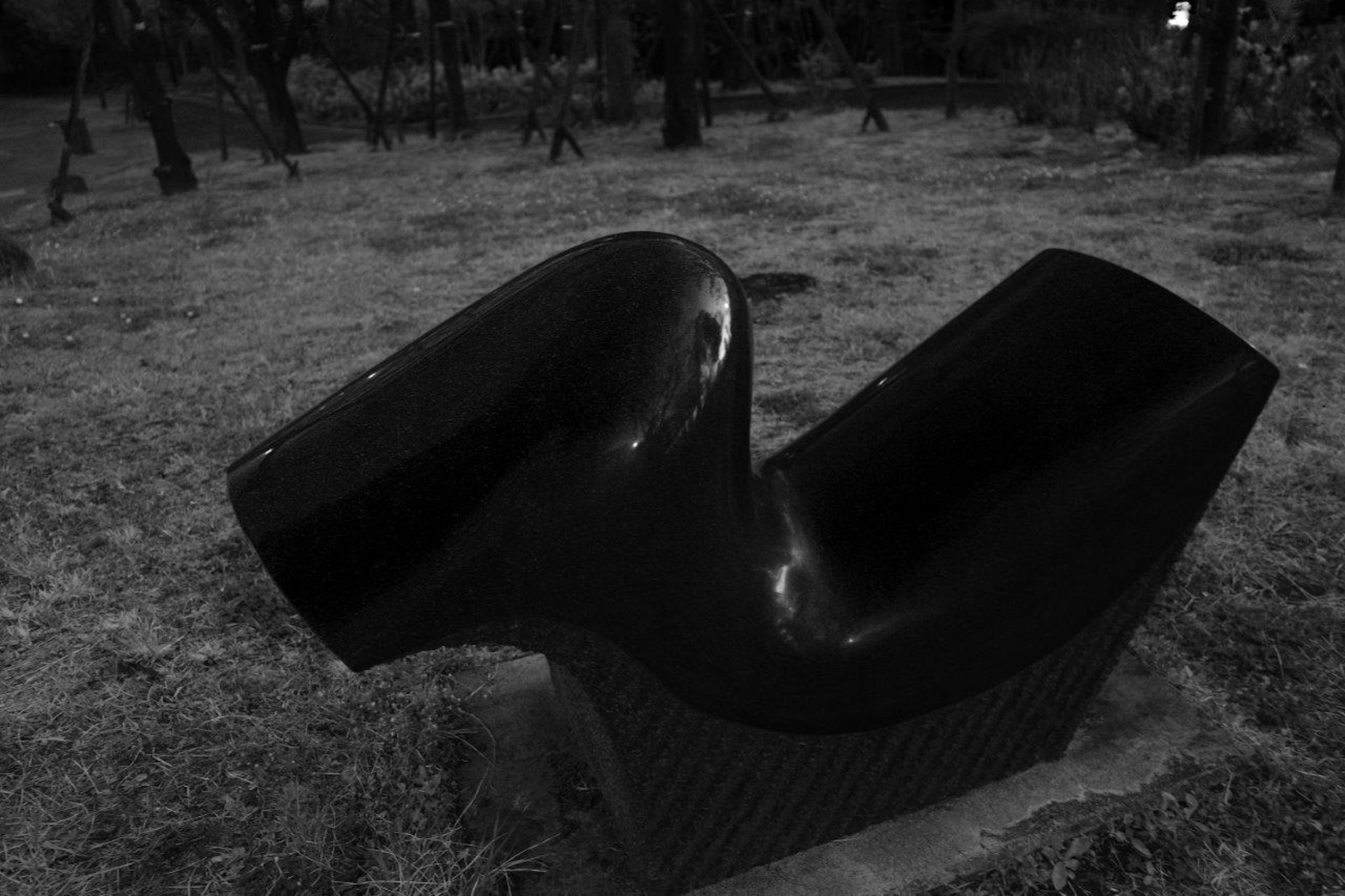 A modern black sculpture resembling a chair placed on grass