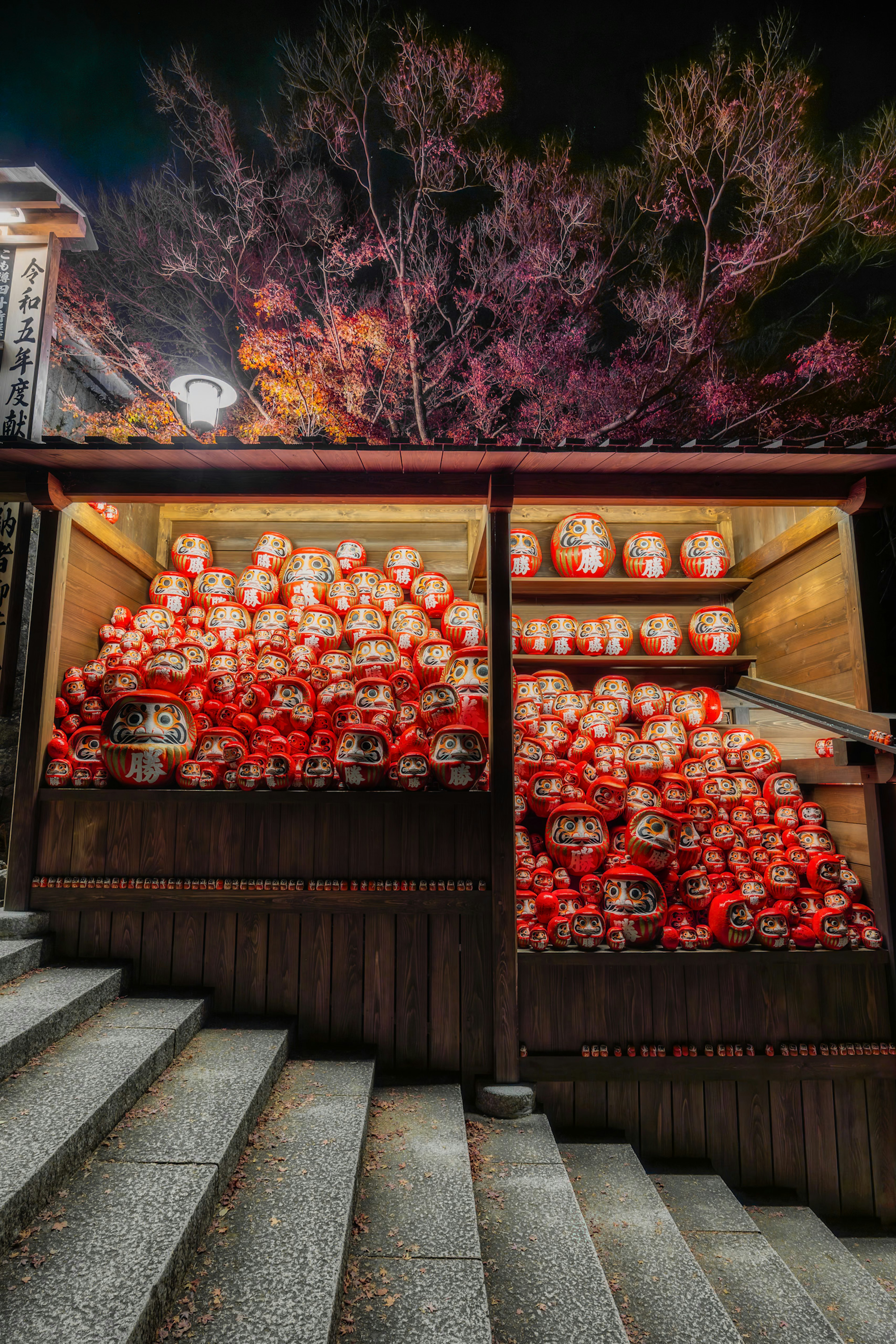 A wooden stall filled with numerous red lanterns at night with a backdrop of illuminated trees