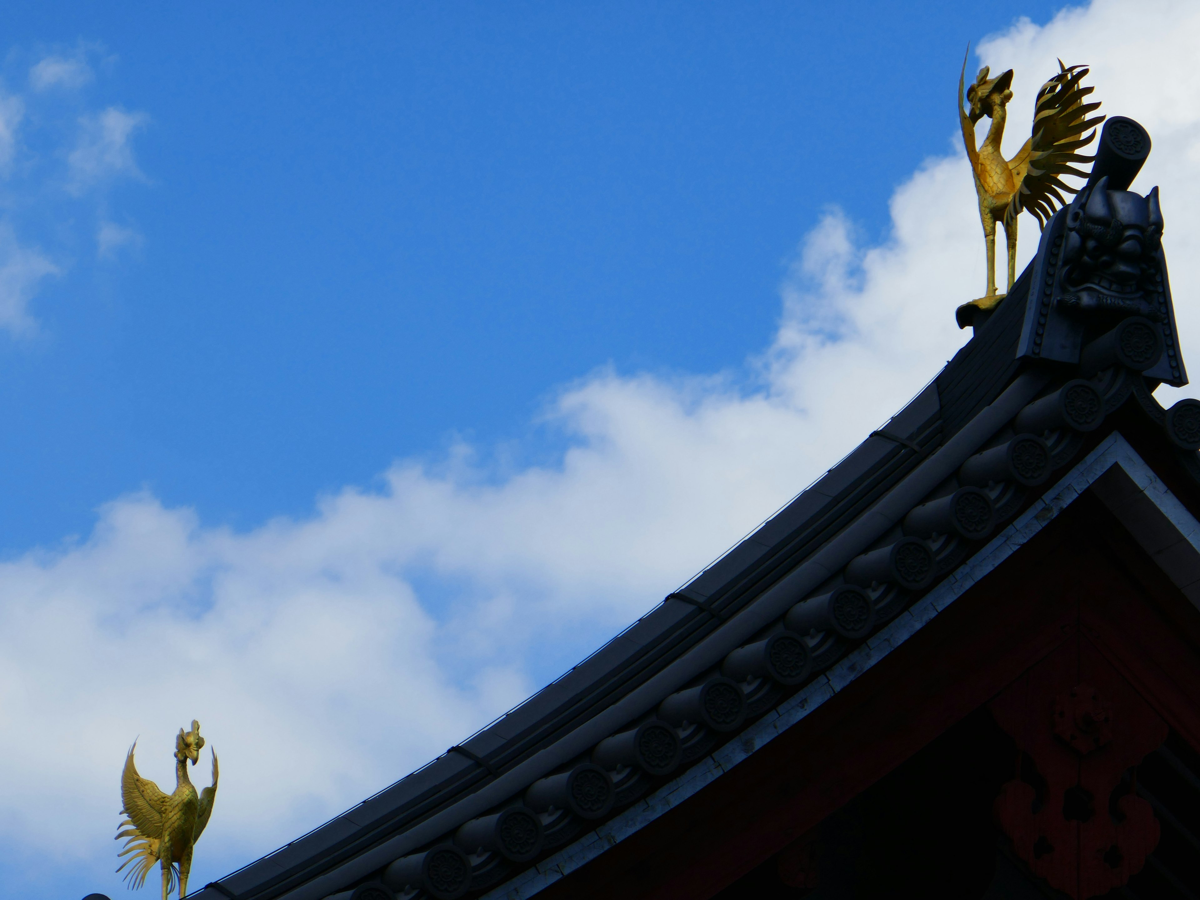 Traditionelles Dach mit goldenen Hahn-Skulpturen vor blauem Himmel