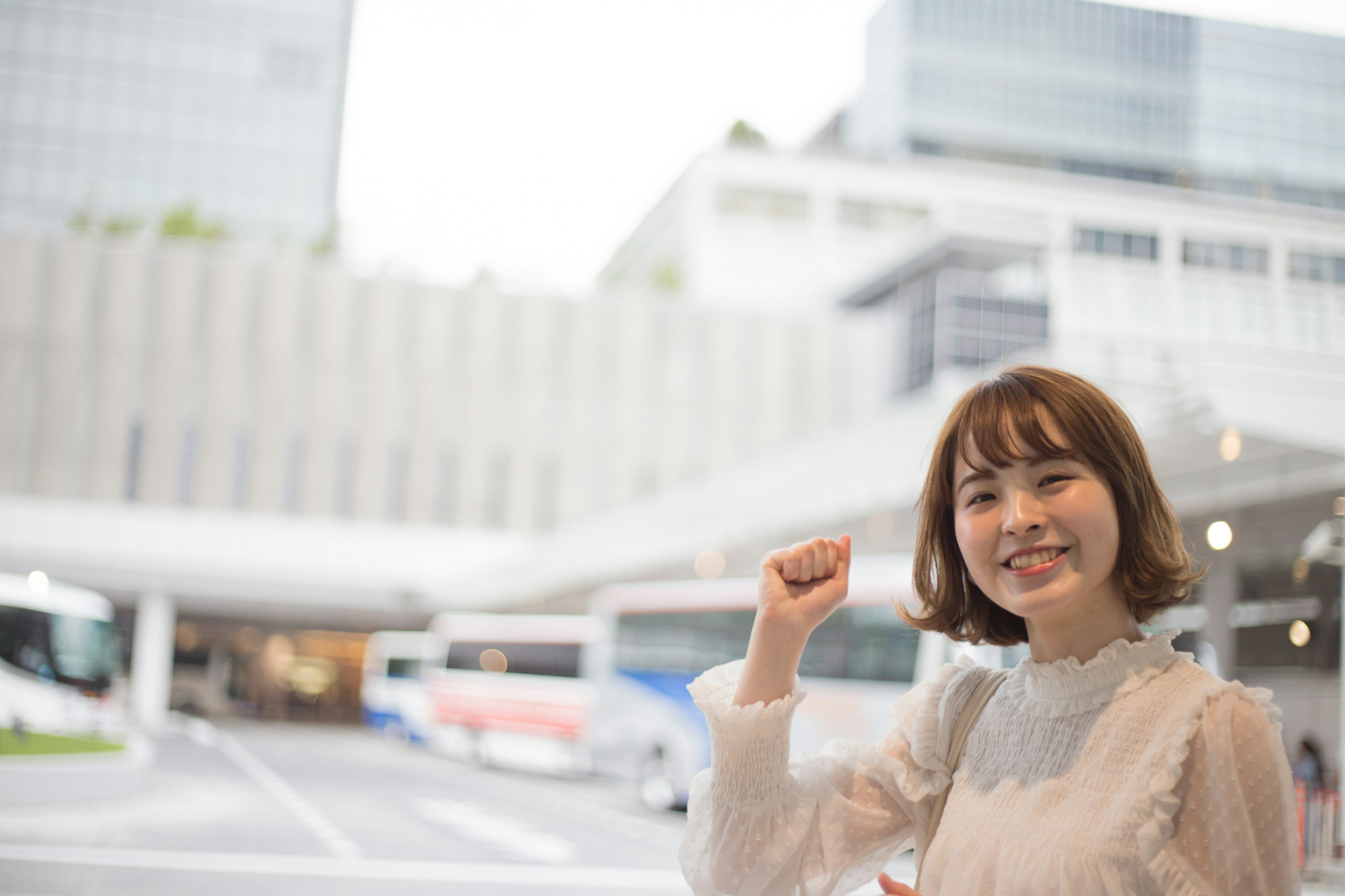 一位微笑的女性举手，背景是公交车站和建筑