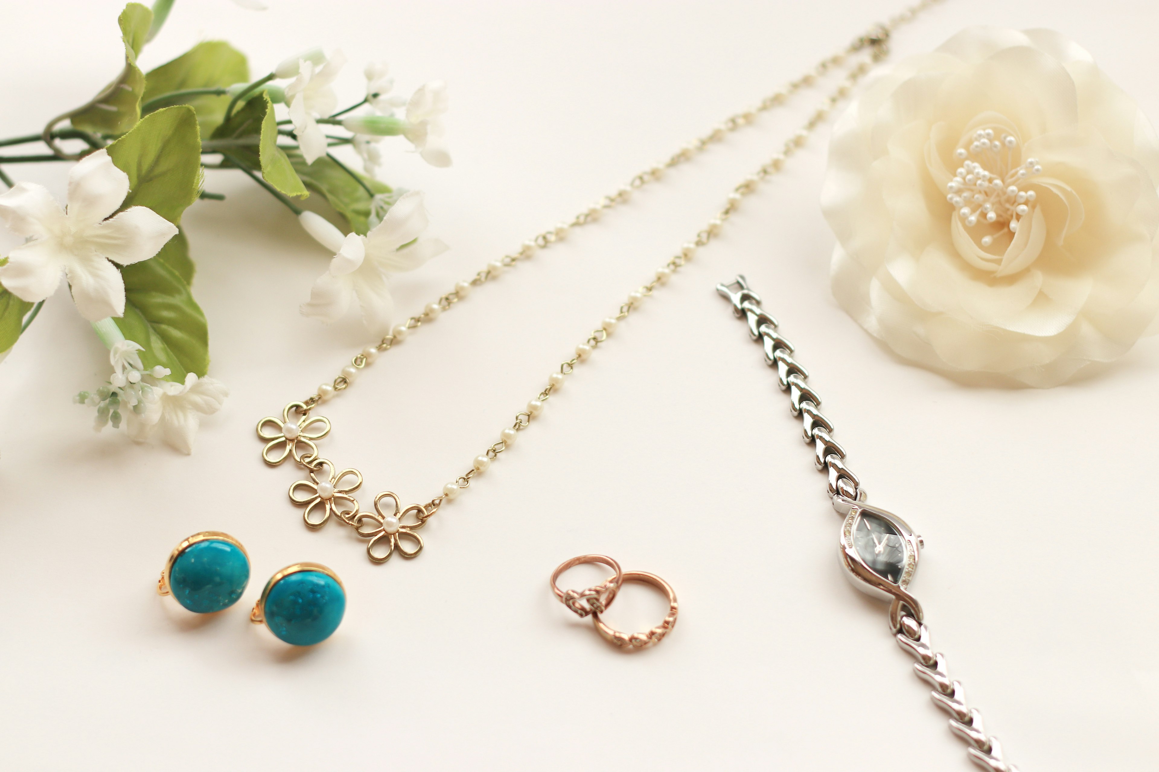 Jewelry arrangement featuring a white flower gold chain necklace blue earrings silver bracelet rose gold rings