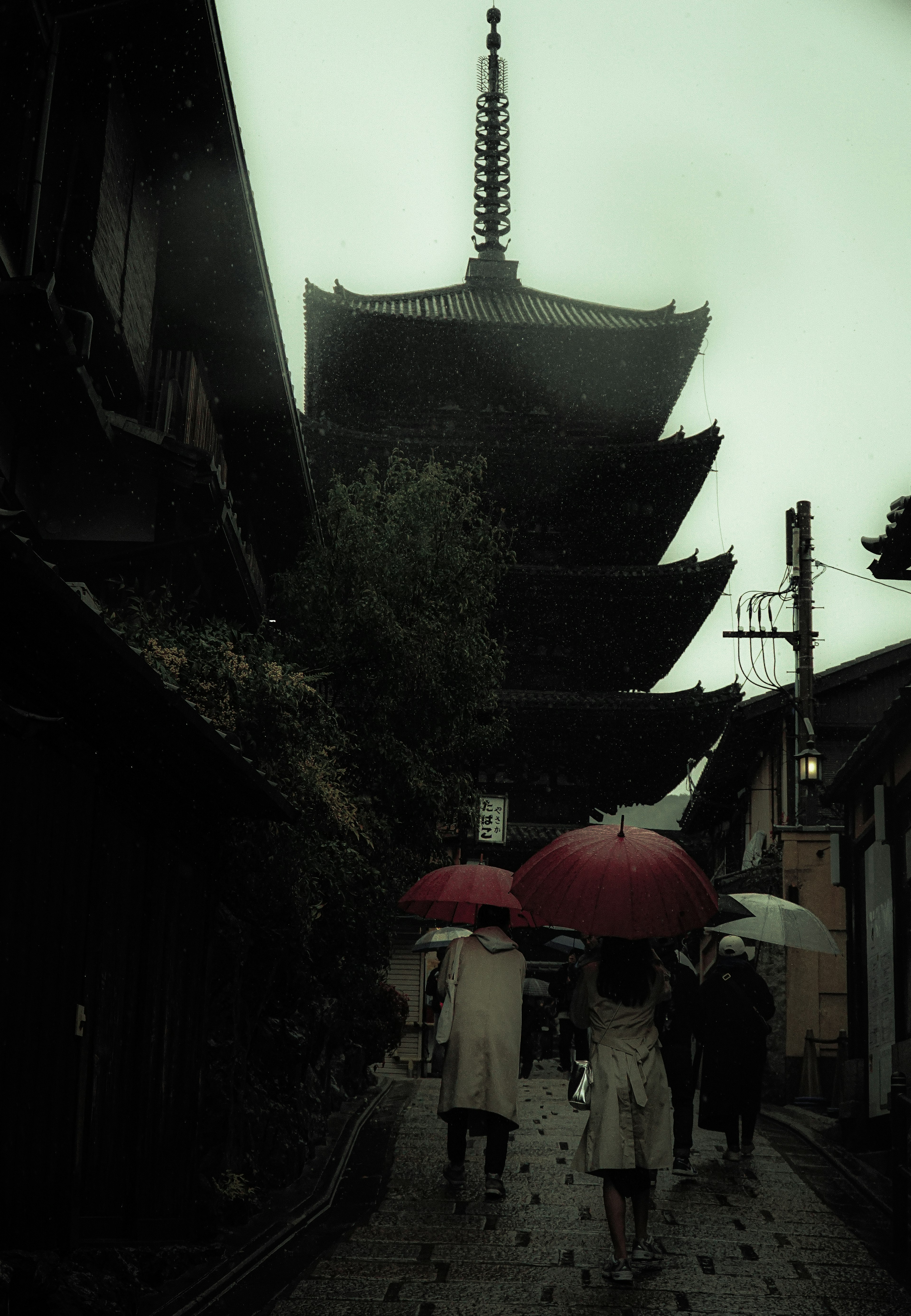 雨の中の五重塔と傘を持つ人々のシルエット