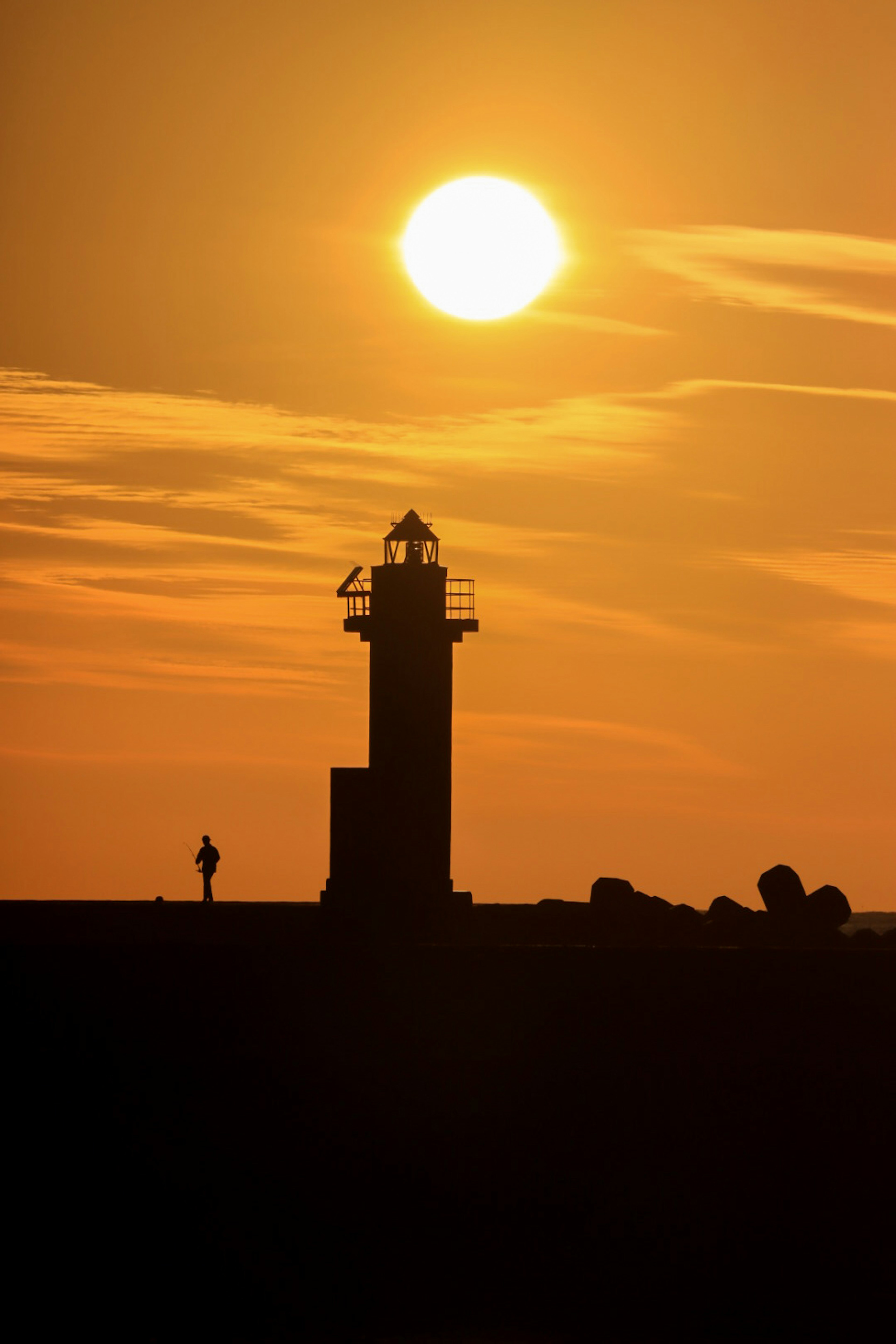 Silhouette of a lighthouse and a person against a sunset