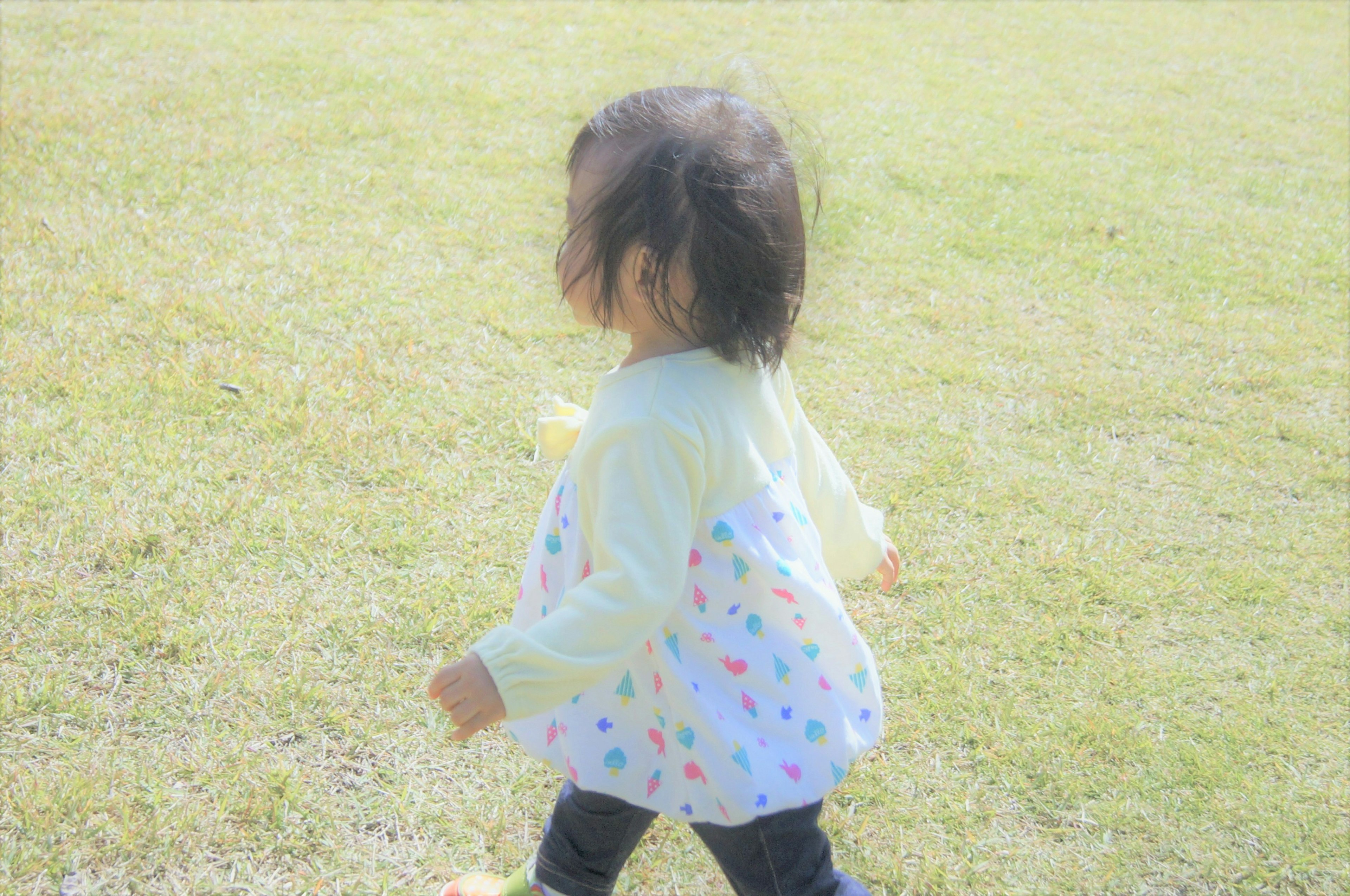 Child walking on grass wearing a colorful polka dot shirt