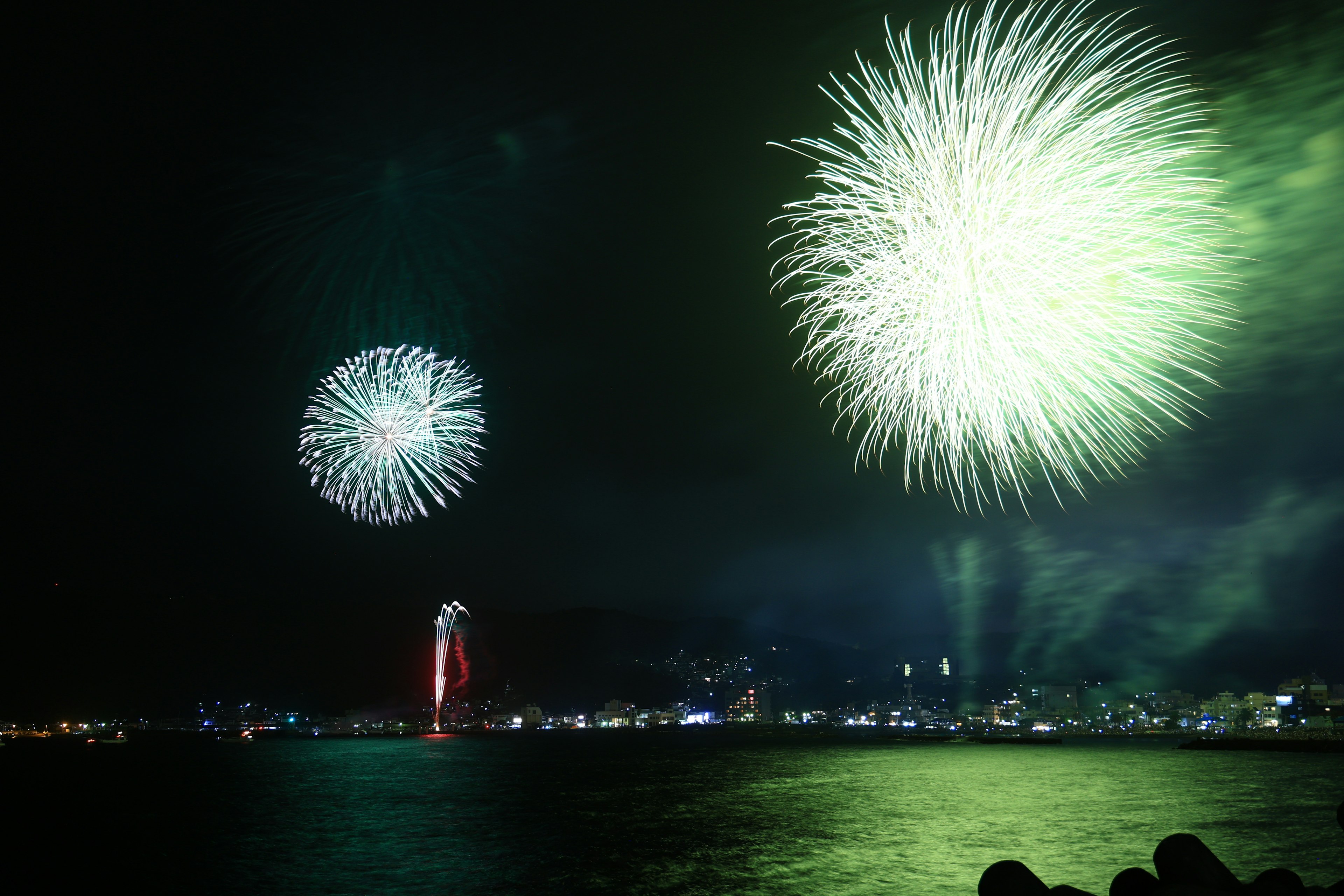 Feux d'artifice illuminant le ciel nocturne au-dessus d'une mer réfléchissante